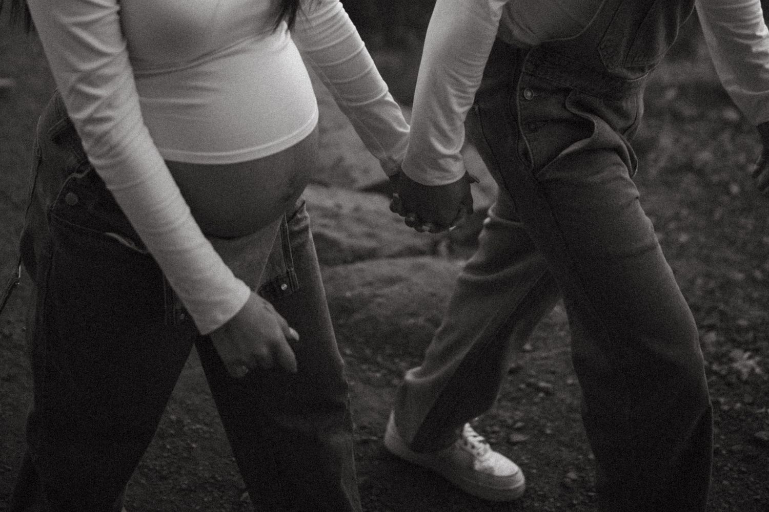 A black and white photograph showing two people holding hands while walking.