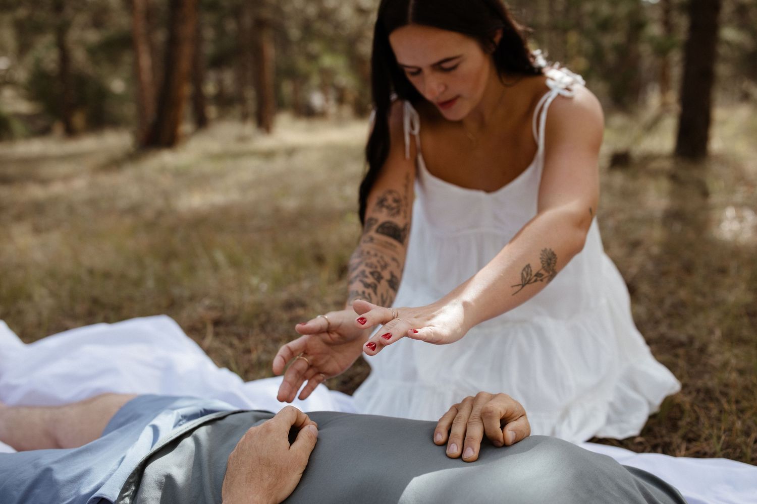 Person in white dress performing a healing ritual outdoors with stones and crystals.
