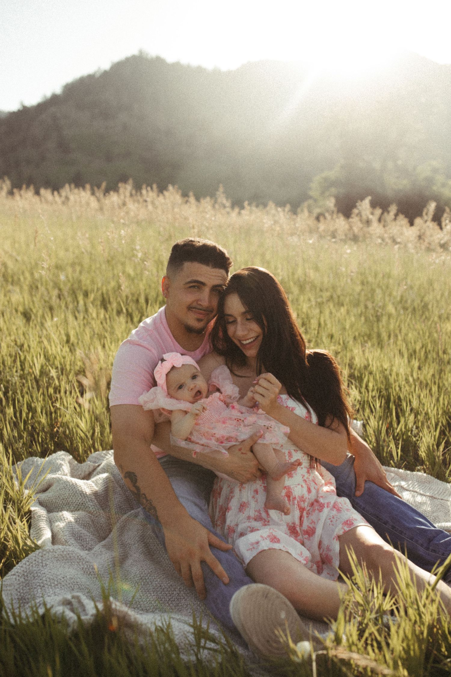 Family shares tender moments together on a blanket in a sunlit meadow.