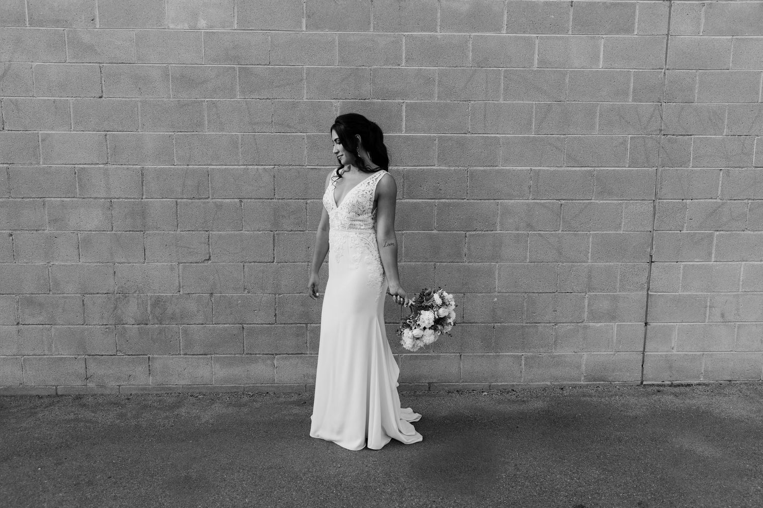 Minimalist black and white bridal portrait with flowing dress against concrete wall.