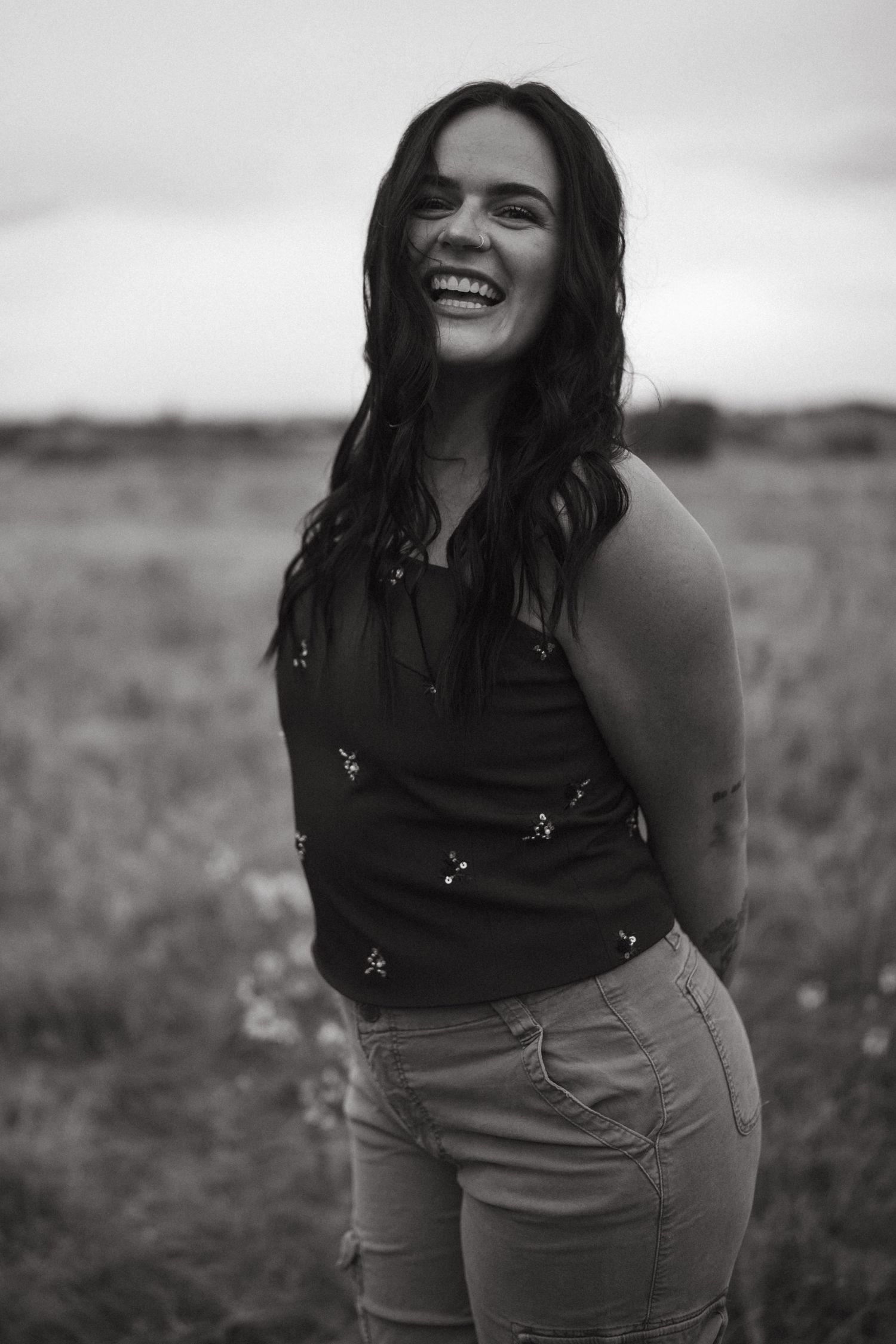 A candid black and white portrait of someone laughing outdoors.