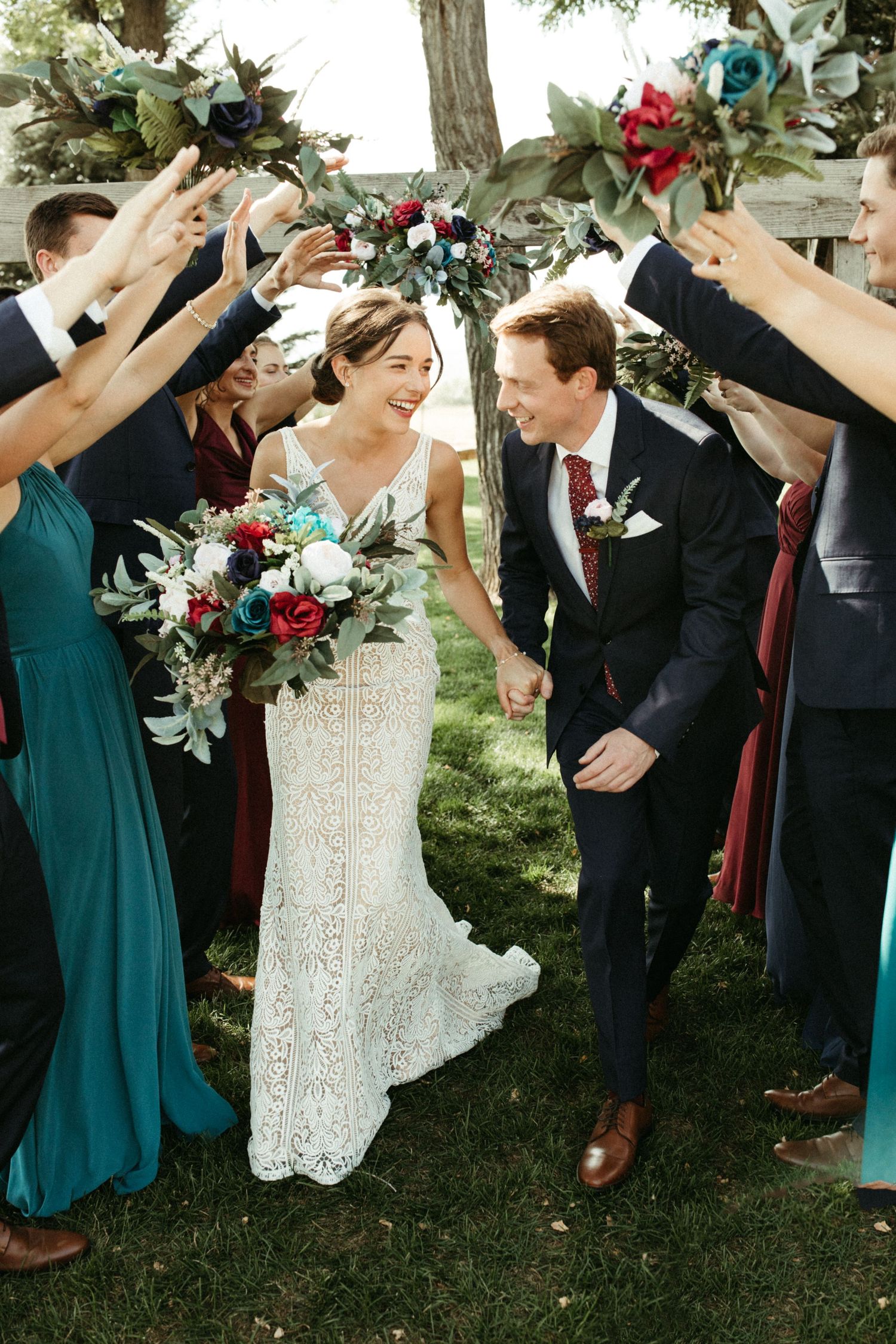 A joyful wedding celebration with bridesmaids in teal dresses forming a tunnel for the newlyweds.