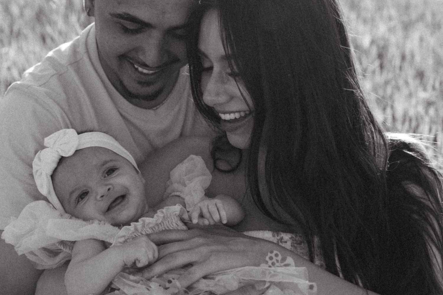 Black and white portrait of parents sharing joyful moment with baby outdoors.