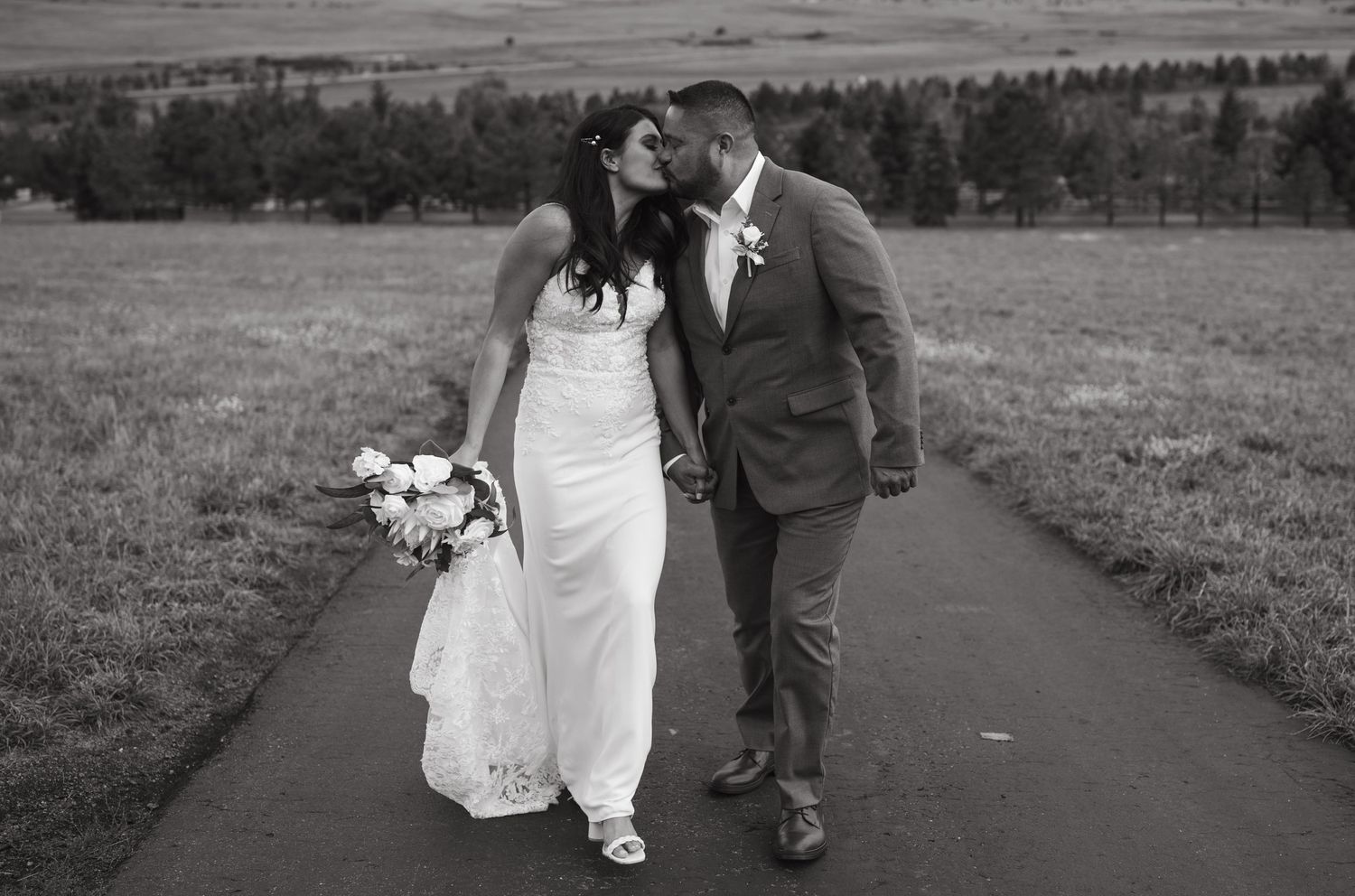 Black and white portrait of couple walking together on mountain path during wedding photoshoot.