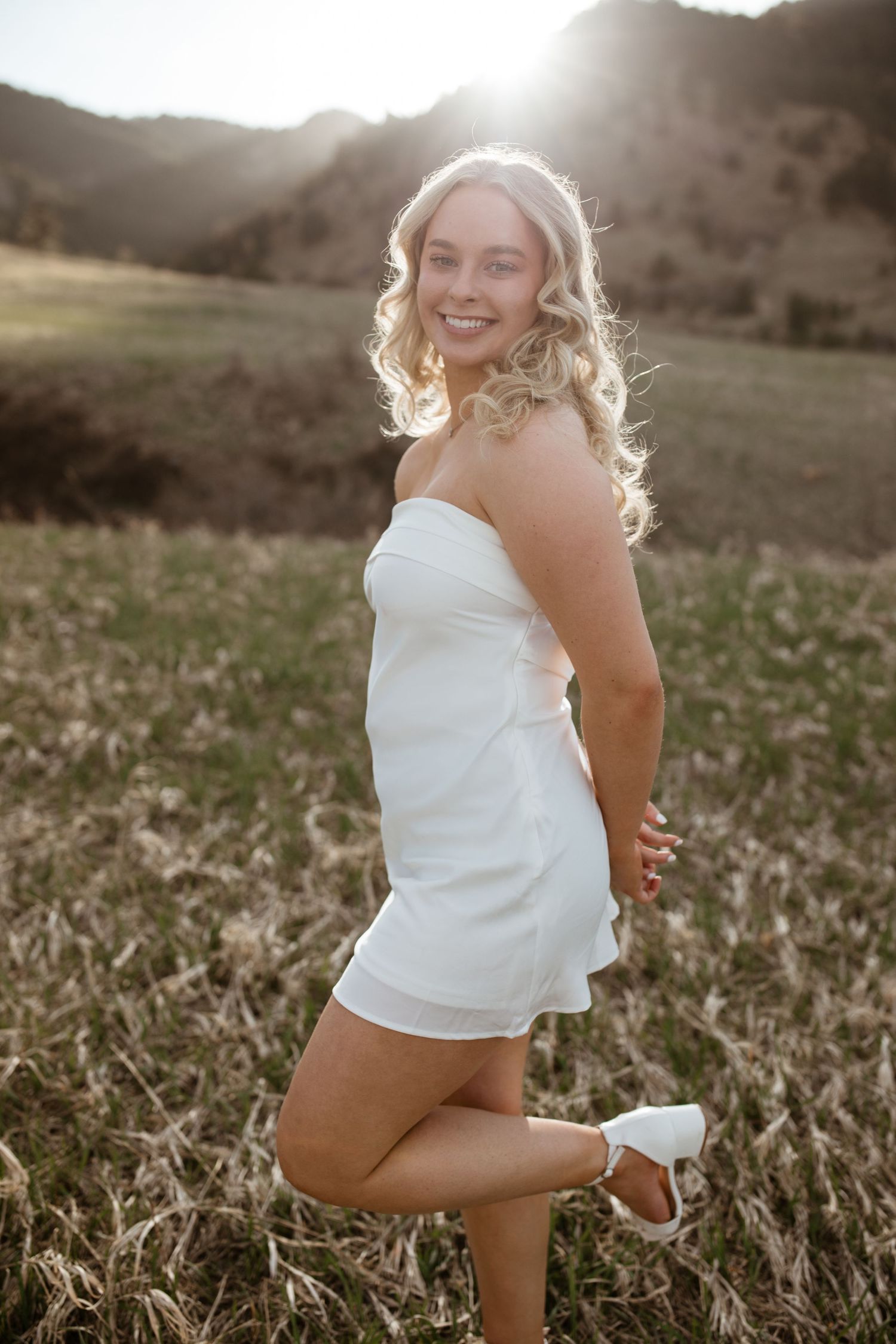 A child in a white tank top playing in a grassy field at sunset with warm golden backlighting.