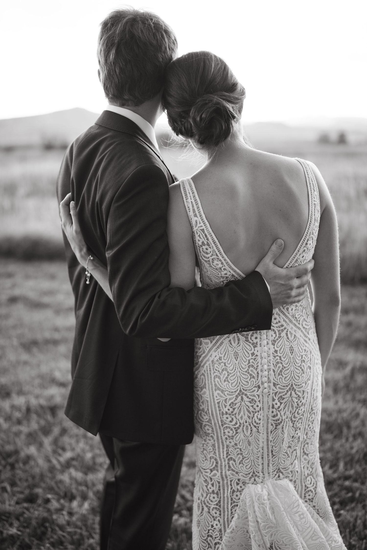 A black and white photo captures a tender moment between newlyweds overlooking a scenic landscape.