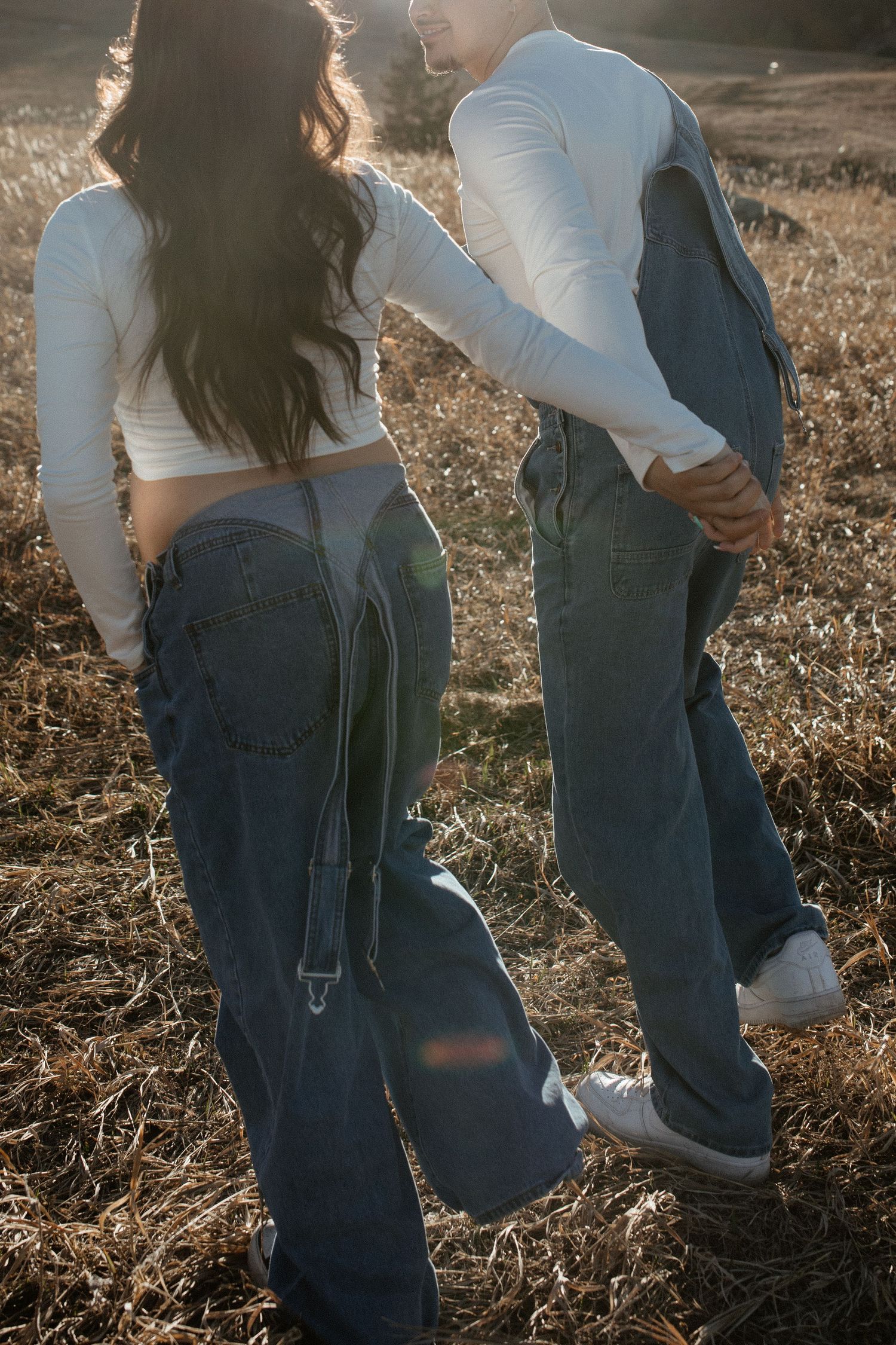 Stylish maternity photoshoot featuring couple in matching denim and white tops in golden sunlight.