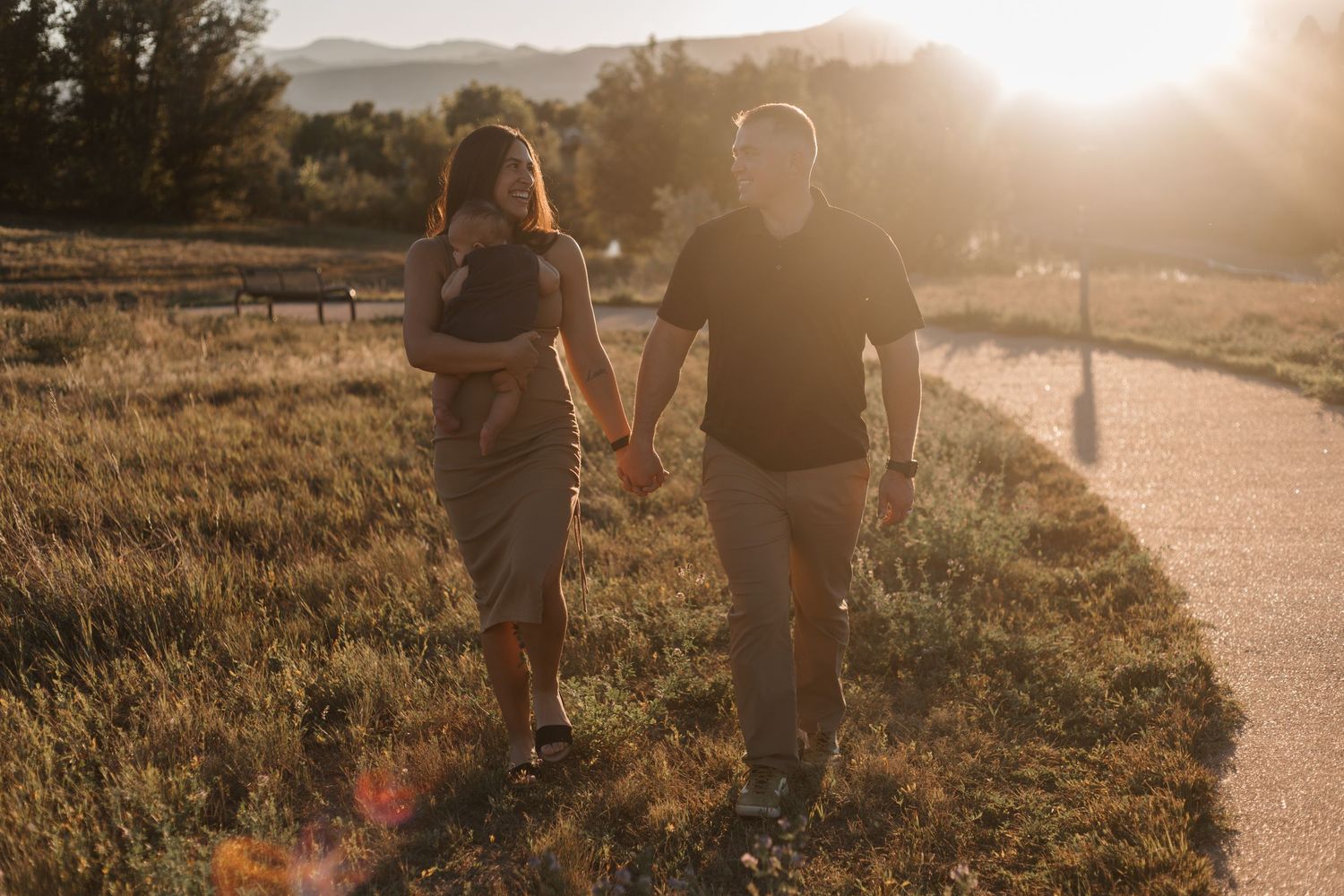Couple walking hand in hand on a path during sunset in a scenic countryside setting.