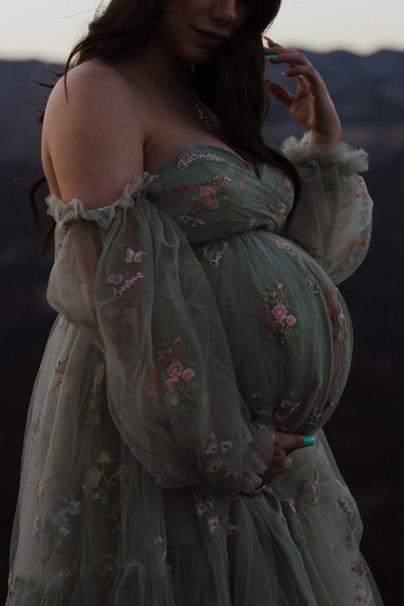 Close-up shot of mint green floral maternity dress with off-shoulder design at sunset.