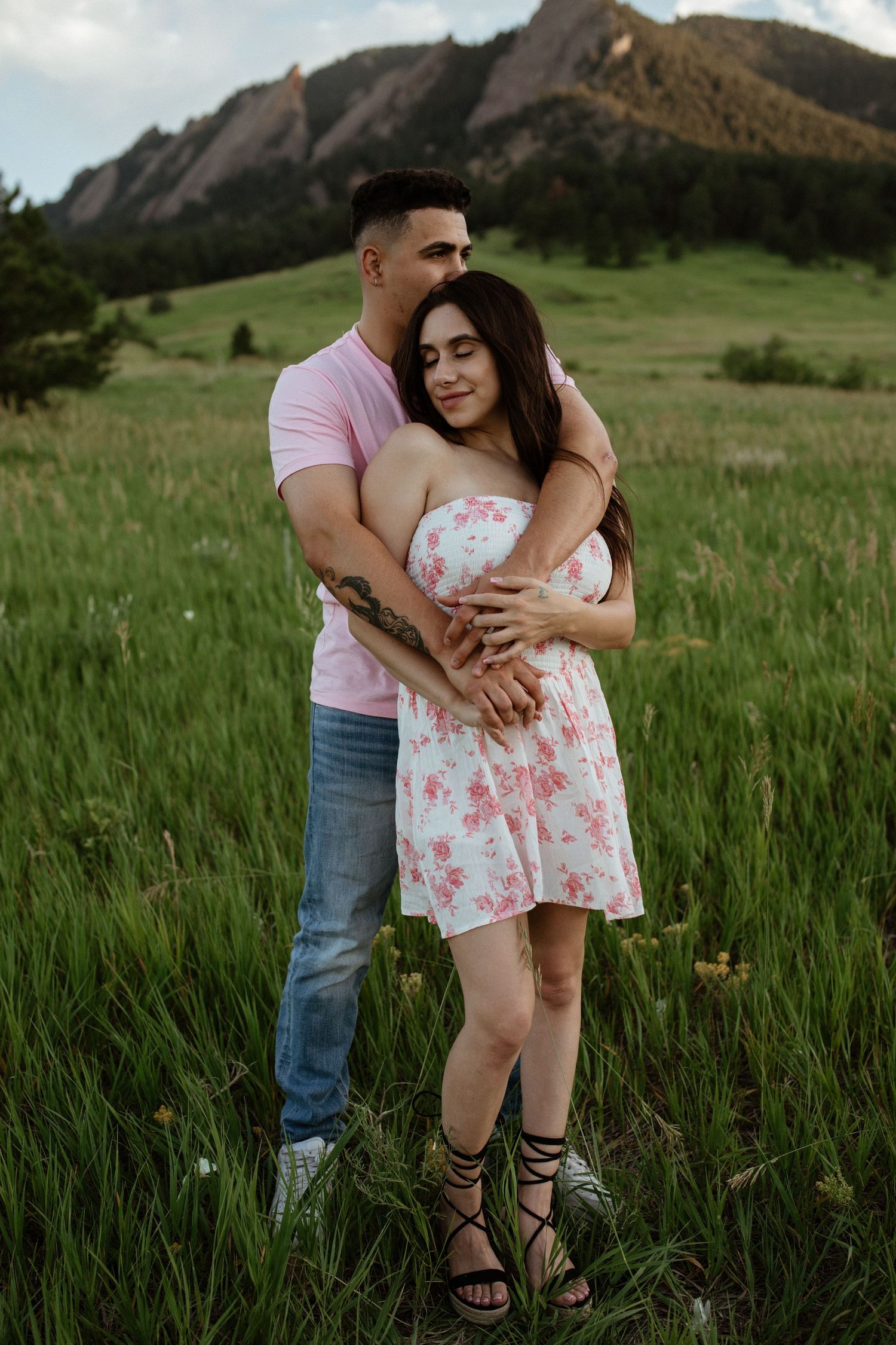 Couple embracing in tall grass with dramatic mountain peaks in the background.