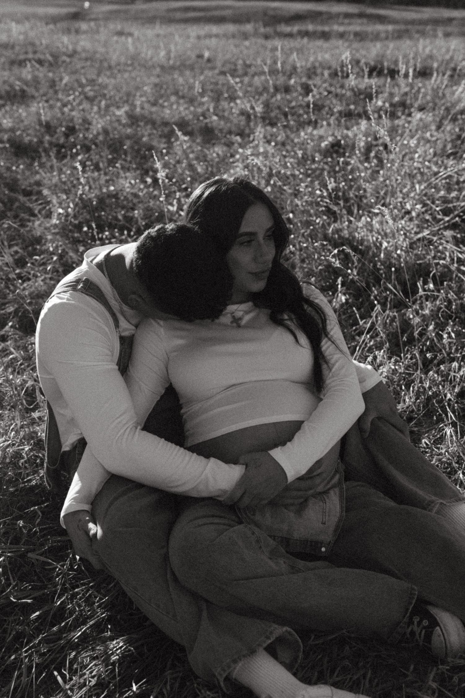 Intimate black and white photo of couple embracing in a grassy field.