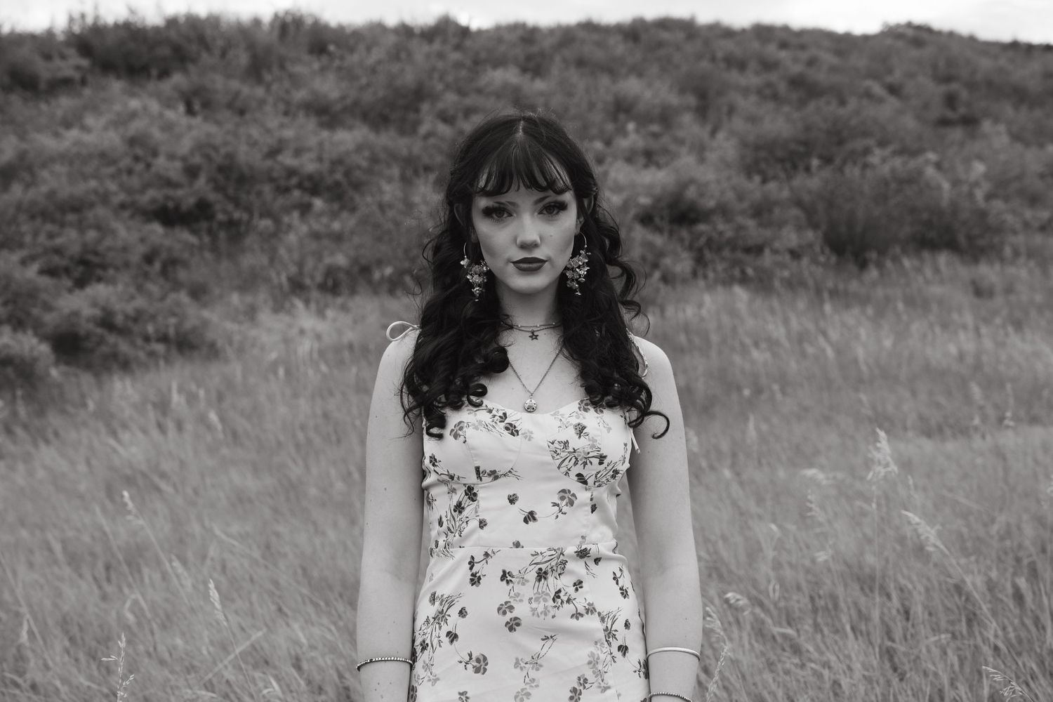 A series of black and white portraits showing someone in a floral dress standing in a grassy field.