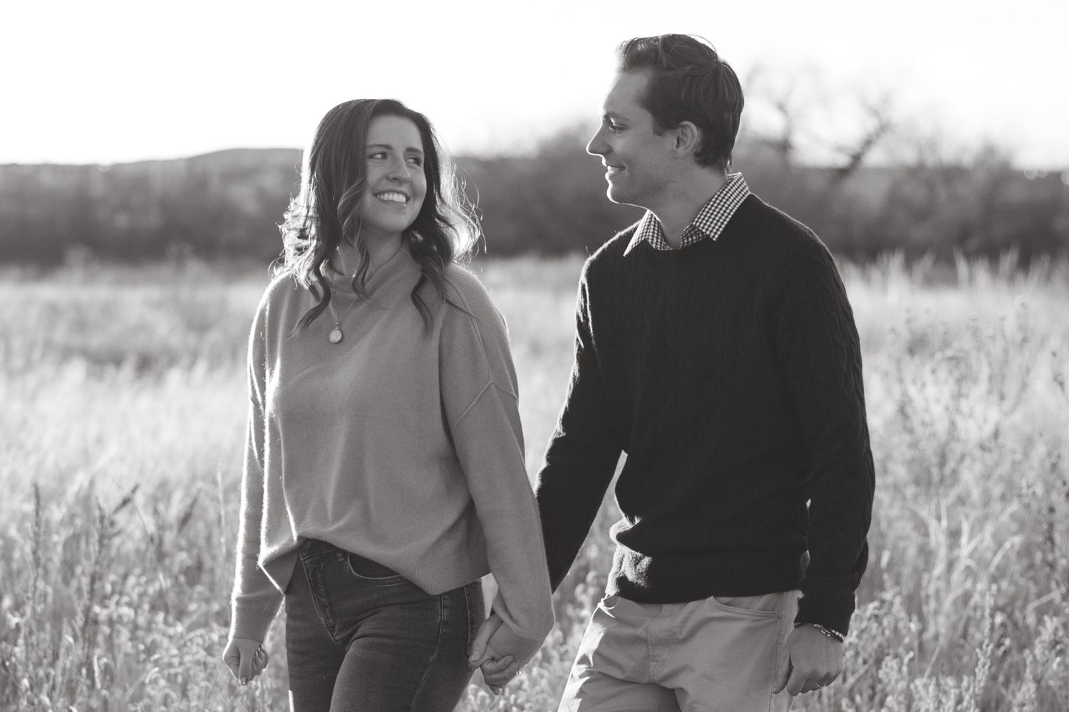A series of candid black and white images showing a couple walking and sharing joyful moments in a sunlit field.