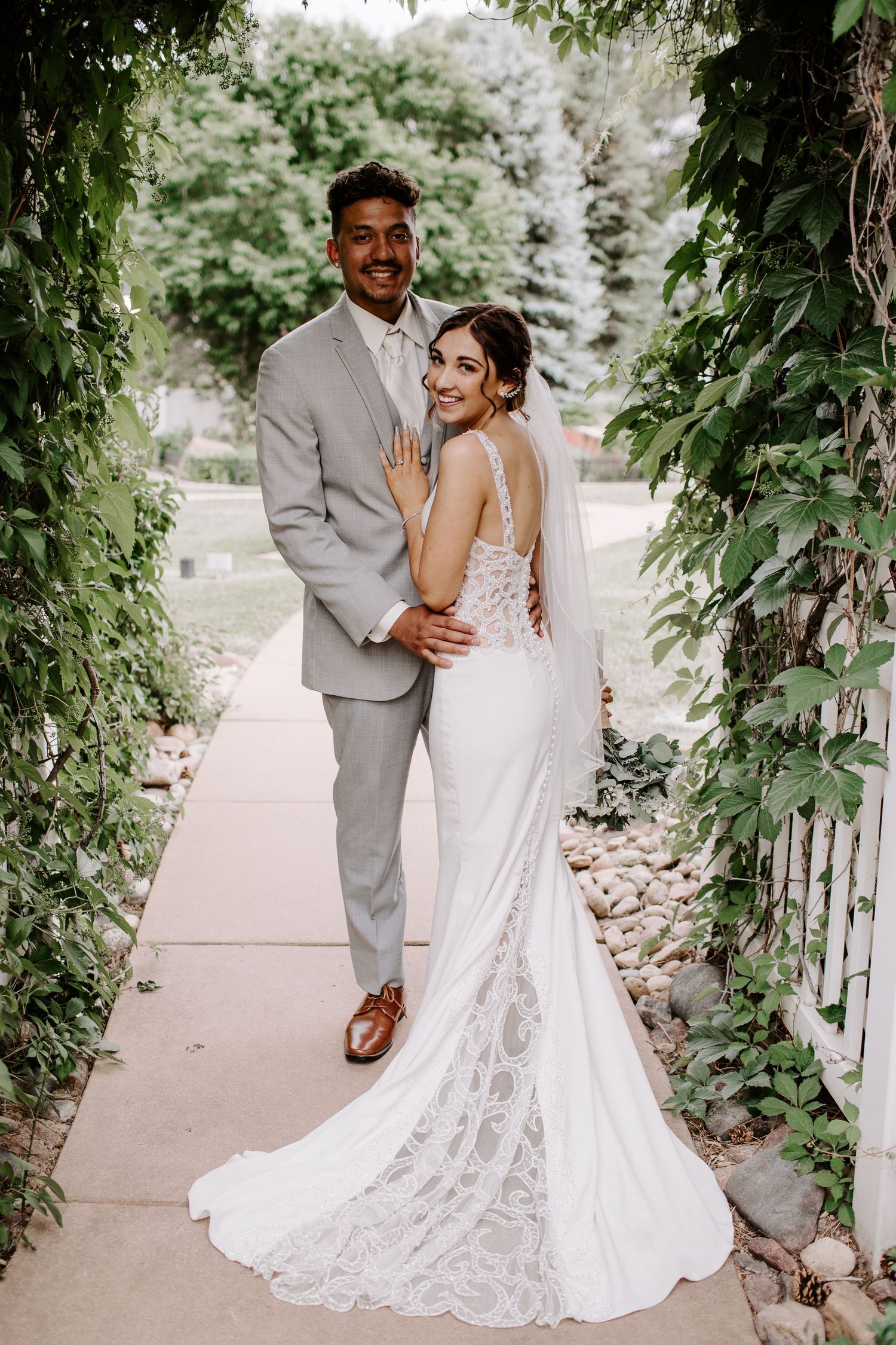Wedding couple posing under an ivy-covered archway in elegant attire.