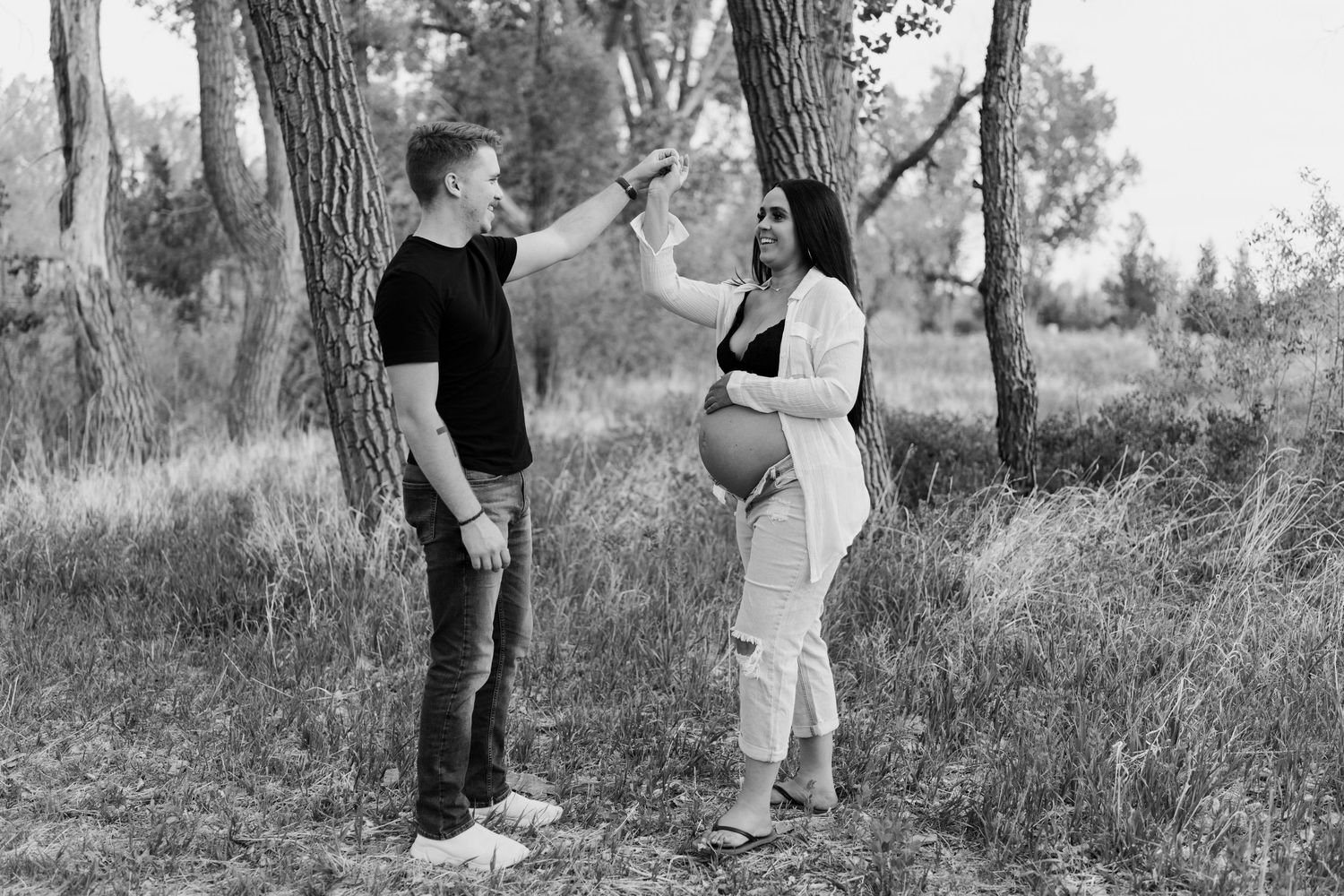 Black and white maternity photo of couple having conversation in wooded setting.