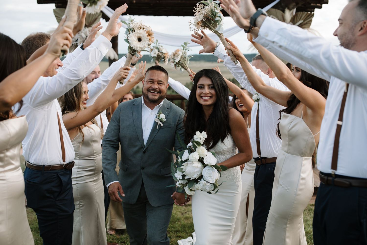 Wedding guests raise their glasses in celebration as the newlyweds walk beneath the toast.