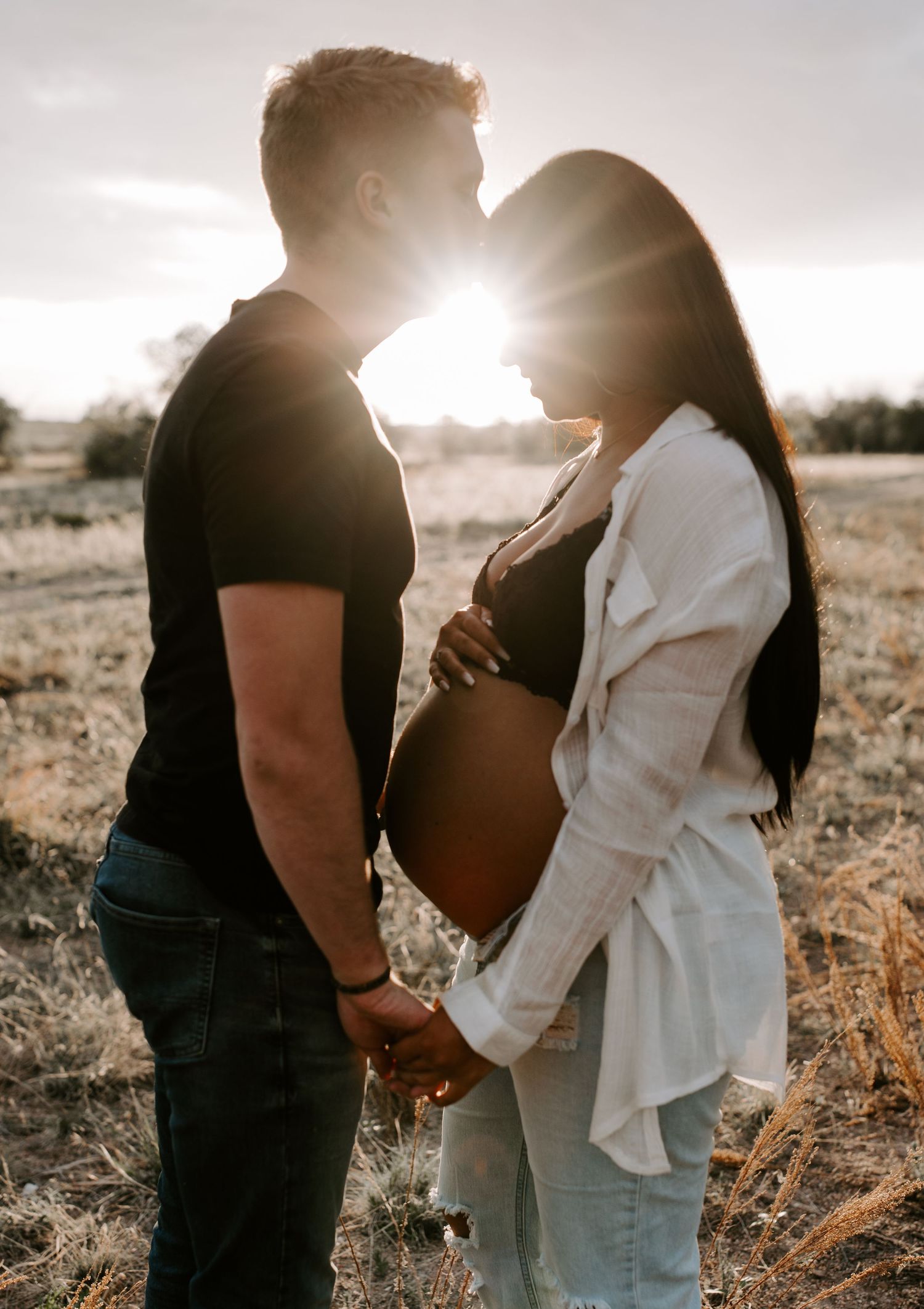 A maternity photo of a couple silhouetted against golden sunlight in a field.
