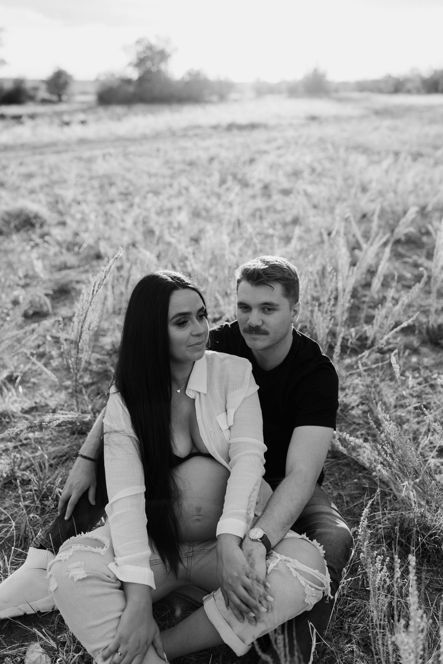 Couple sharing intimate moments together in a sunlit field during a romantic photoshoot.
