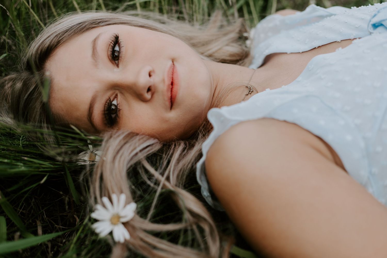 Close up portrait lying in grass with daisy flower and soft natural lighting.