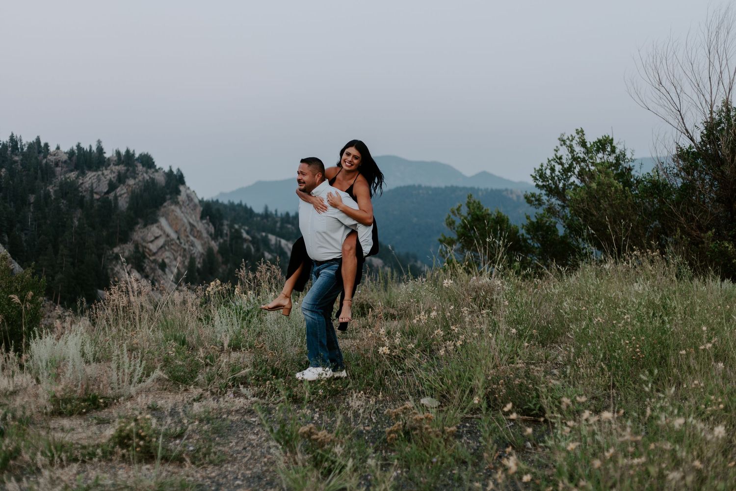 Couple enjoying a playful piggyback ride on a mountain overlook at dusk.