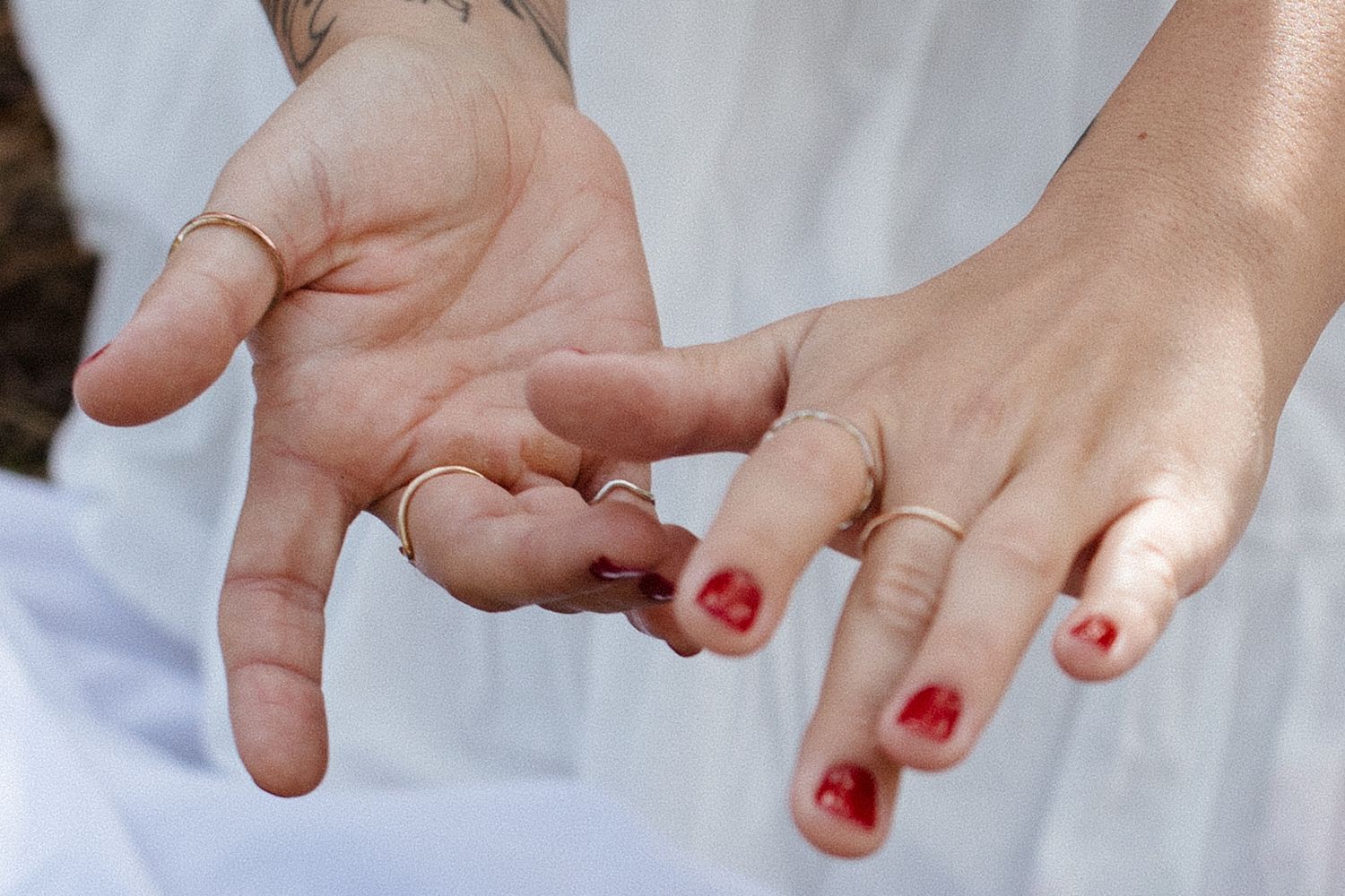 Two hands reaching towards each other with red nail polish visible on the fingernails in soft natural lighting.
