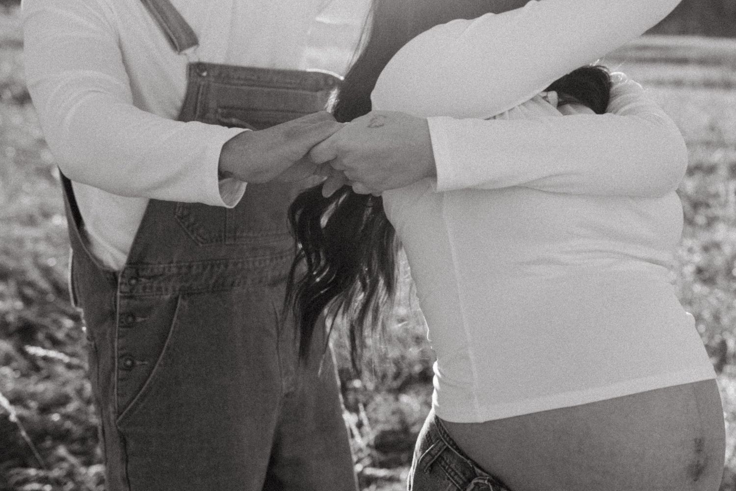 Black and white image of couple holding hands, showing pregnant belly in casual attire.