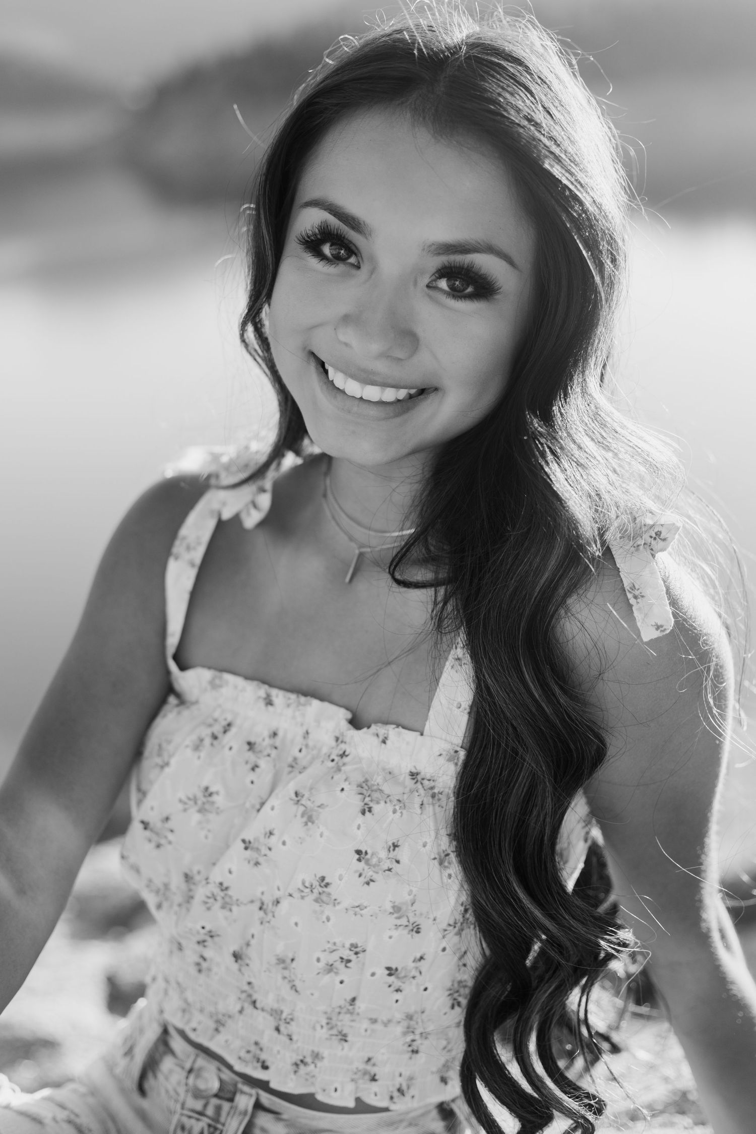Black and white portrait of a woman in a floral top with long dark hair smiling outdoors.