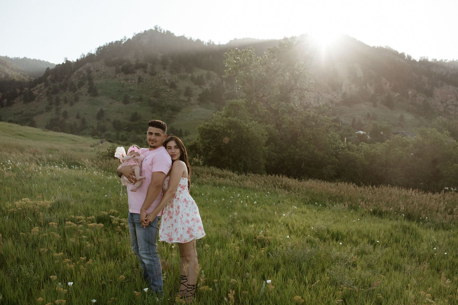 Family standing together in mountain meadow during golden hour sunset.