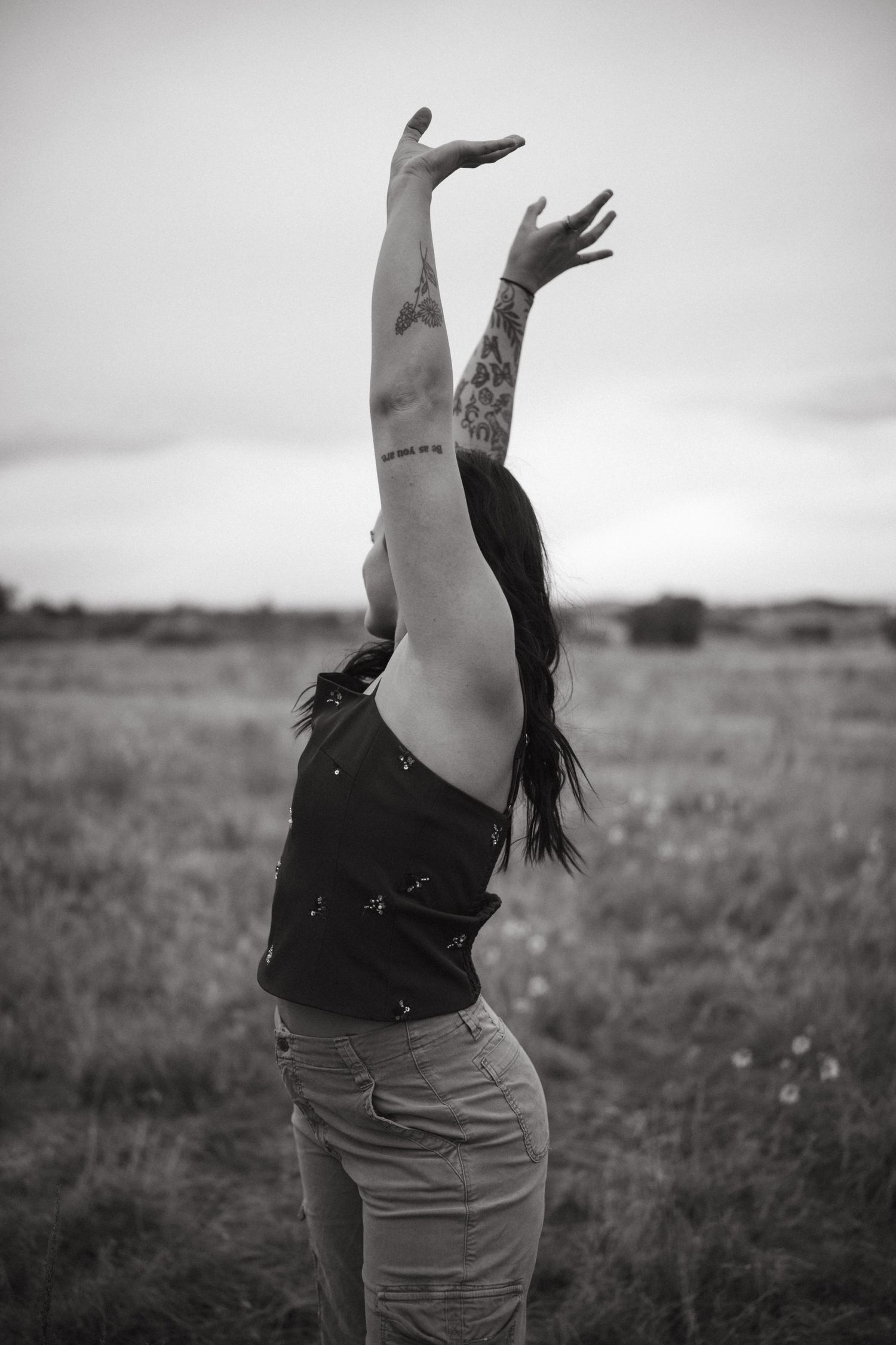 Black and white photo of someone dancing with raised arms in an open field at dusk.