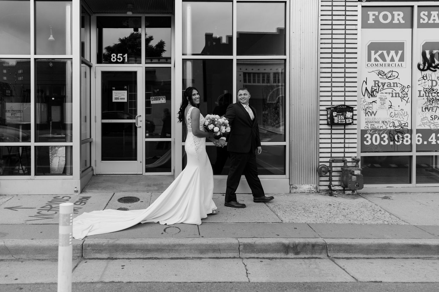 Black and white urban wedding photo outside a storefront with trailing dress.