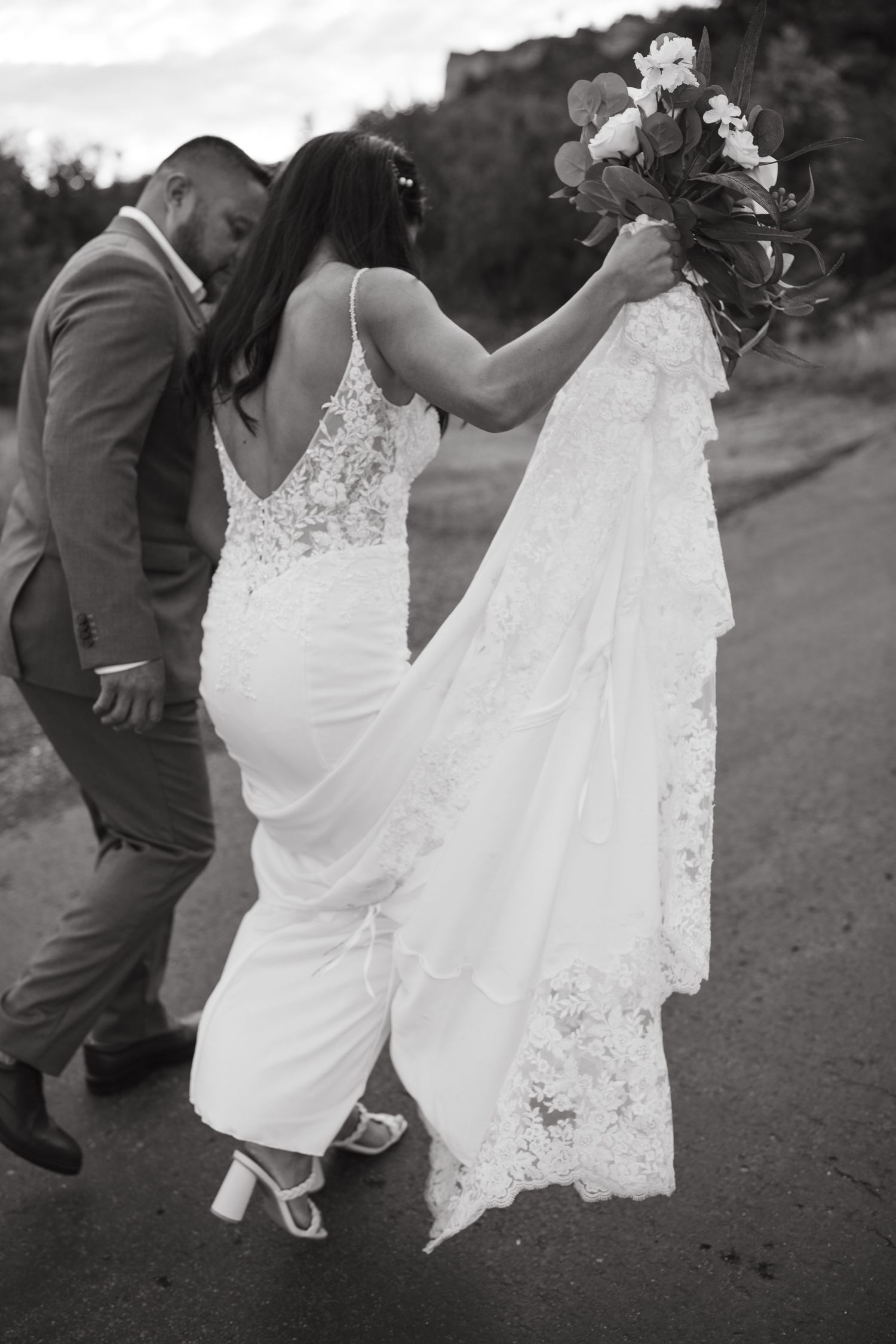 Artistic black and white shot of bride's lace dress train flowing in mountain breeze.