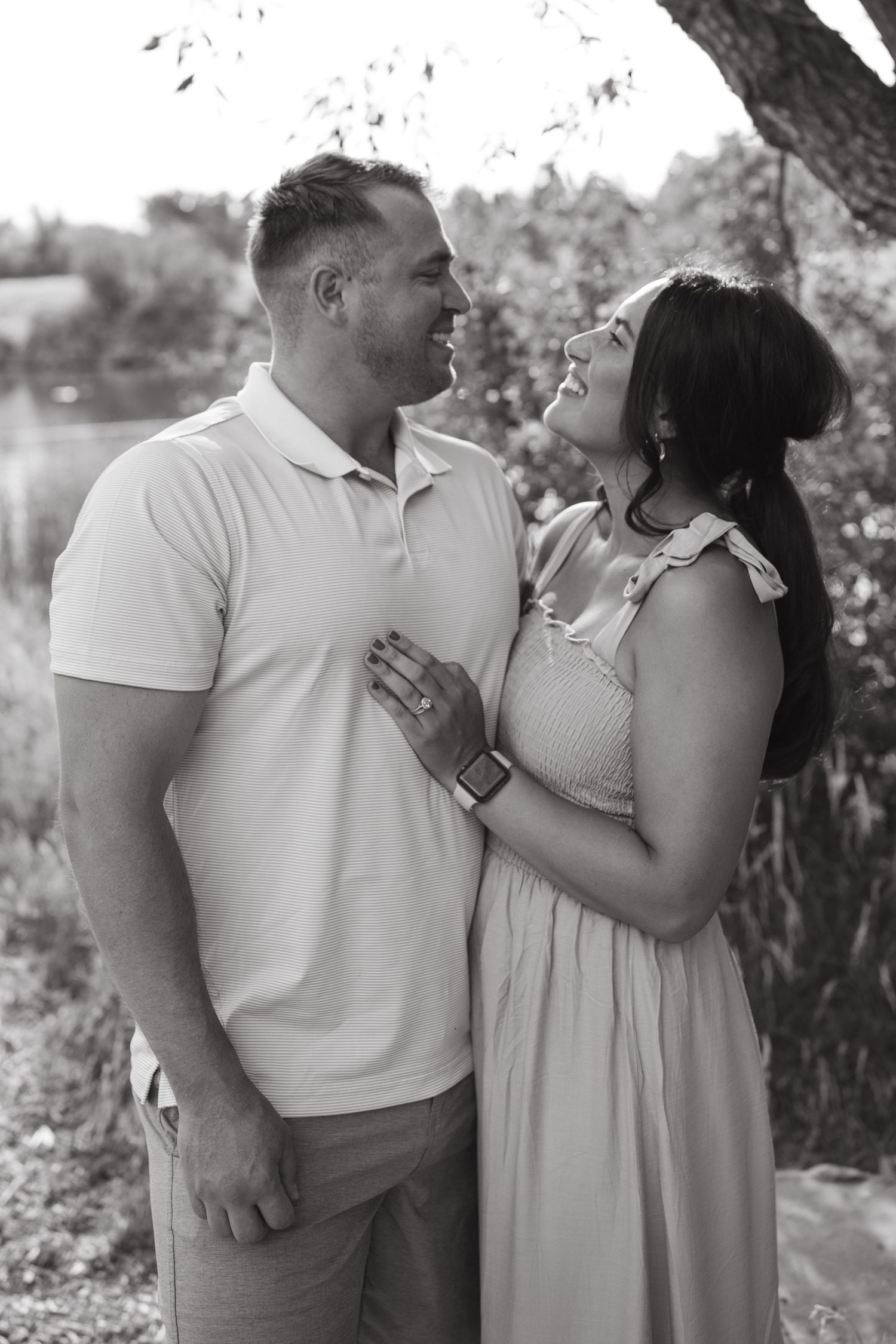 A black and white portrait of a couple gazing at each other outdoors in summer attire.
