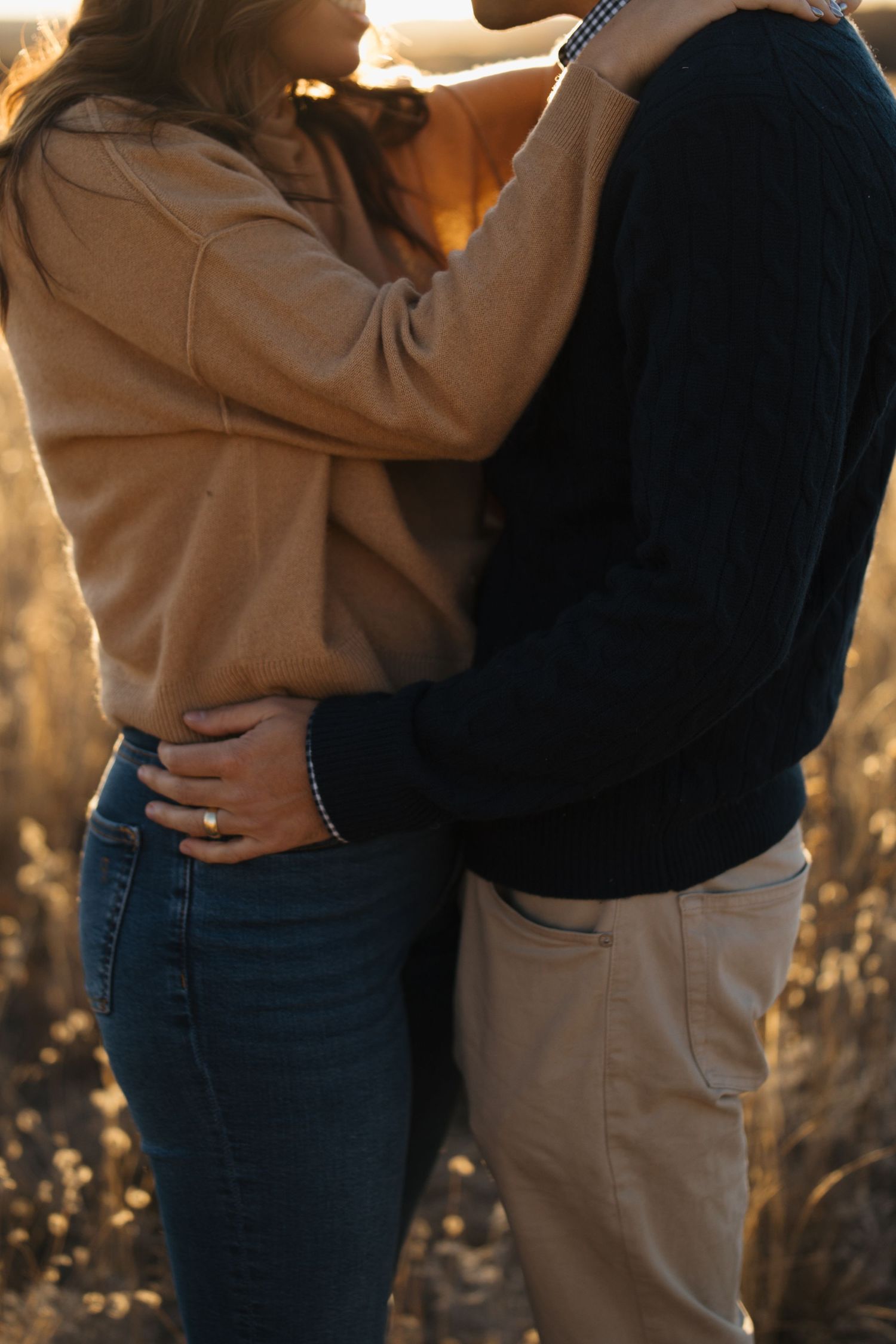 Couple in casual wear embracing during golden hour in a natural outdoor setting.