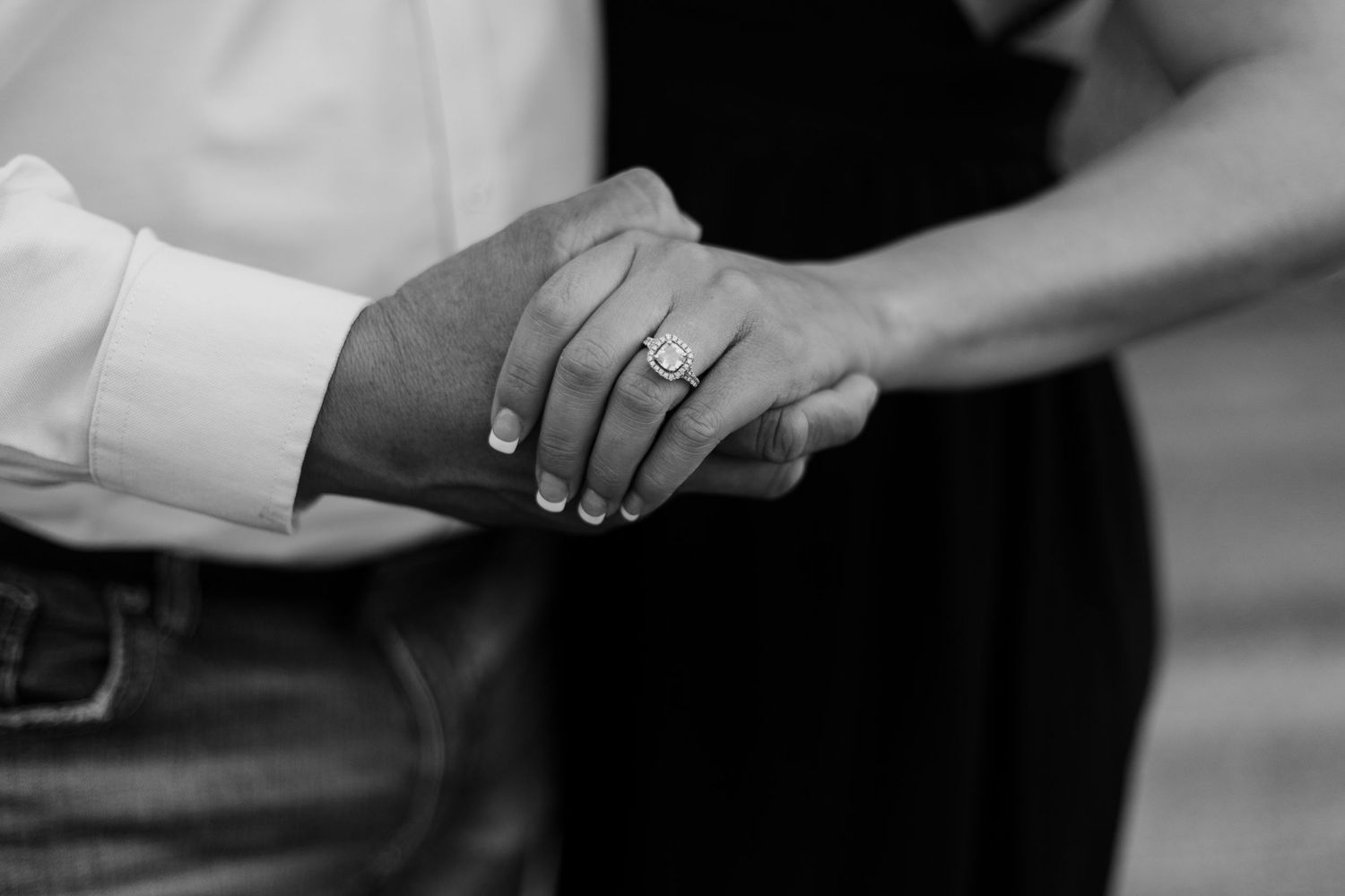A close-up black and white photo of hands with an engagement ring.