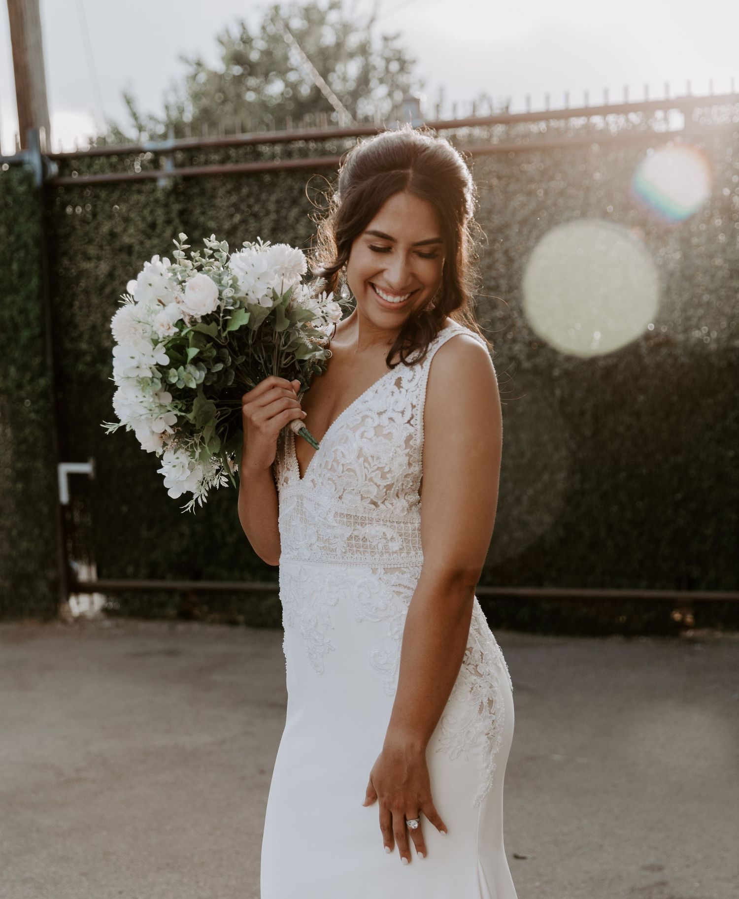 Candid bridal portrait with white bouquet and sunlight flare.