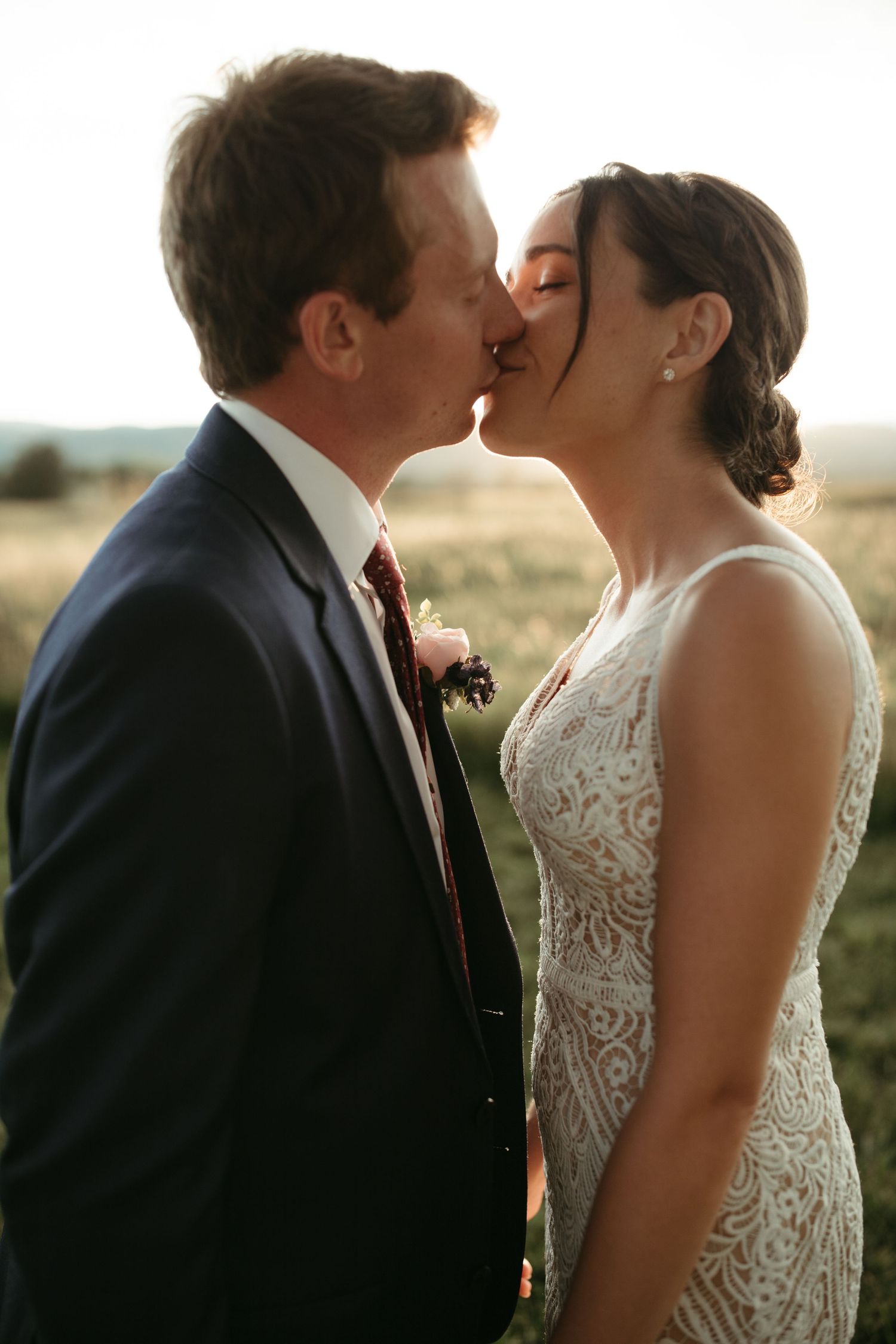 A romantic wedding moment captured in warm sunlight as newlyweds share an intimate kiss.