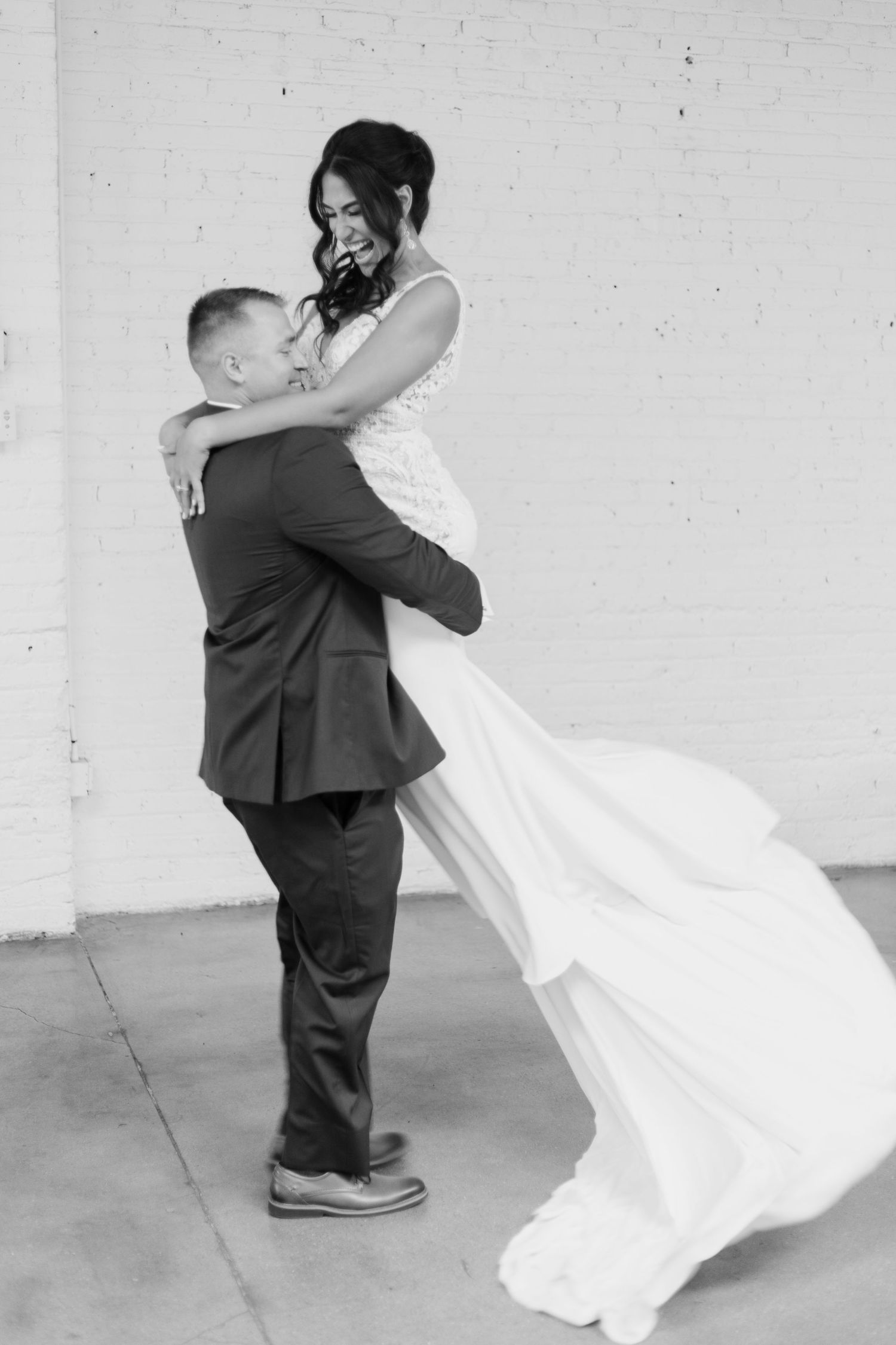 A romantic black and white wedding photo of a couple embracing with the bride's dress flowing in the wind.