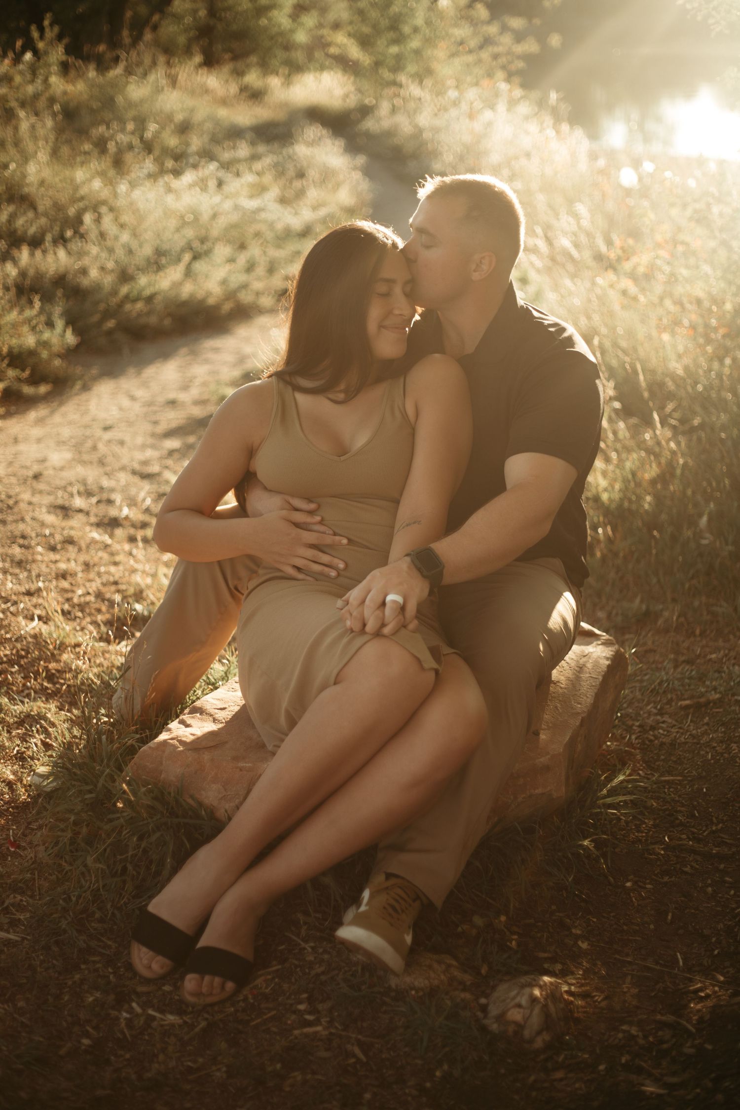 A romantic couple embraces on a path in golden sunlight during a sunset photoshoot.