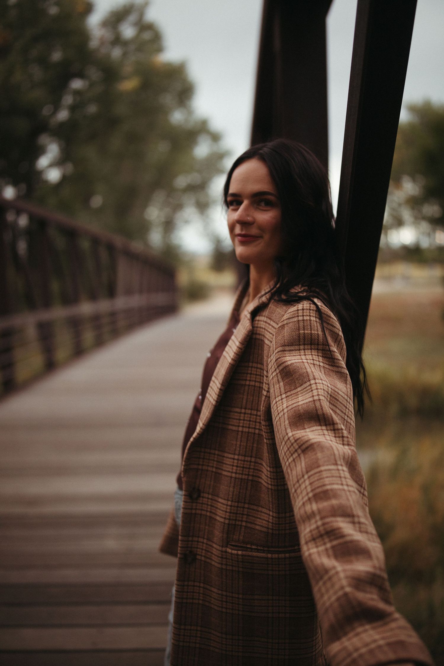 A person in a brown plaid coat stands on a wooden bridge during autumn.