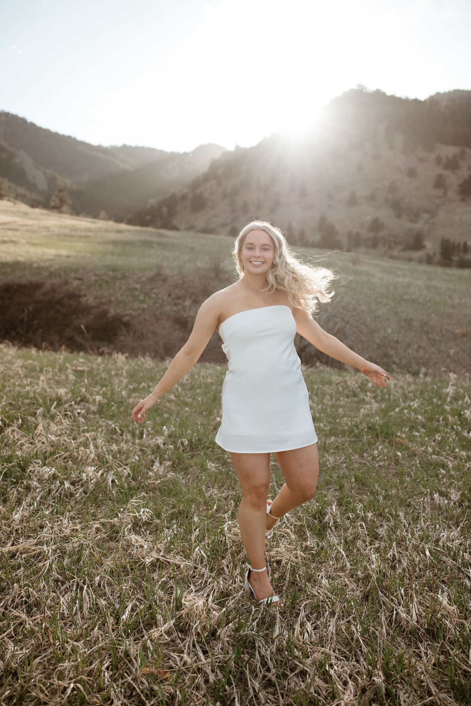 Woman in white dress dancing in sunlit mountain meadow.