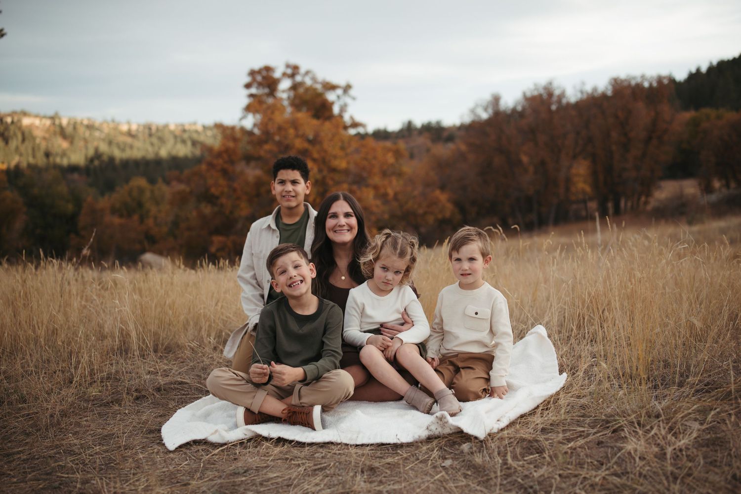 Family relaxing together on a white blanket in golden autumn field.