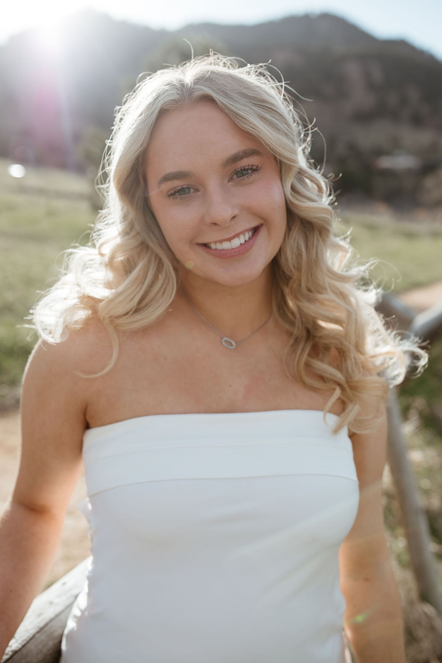 Portrait of woman in white dress with mountains and sunlight behind her.