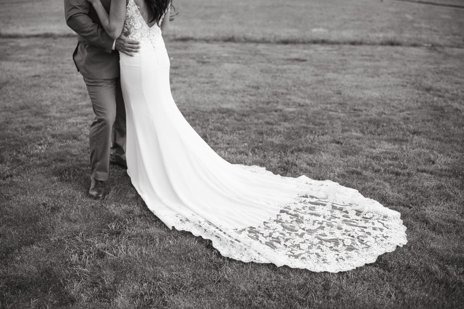 Detail shot of a bride's lace wedding dress train trailing on grass with mountains in background.