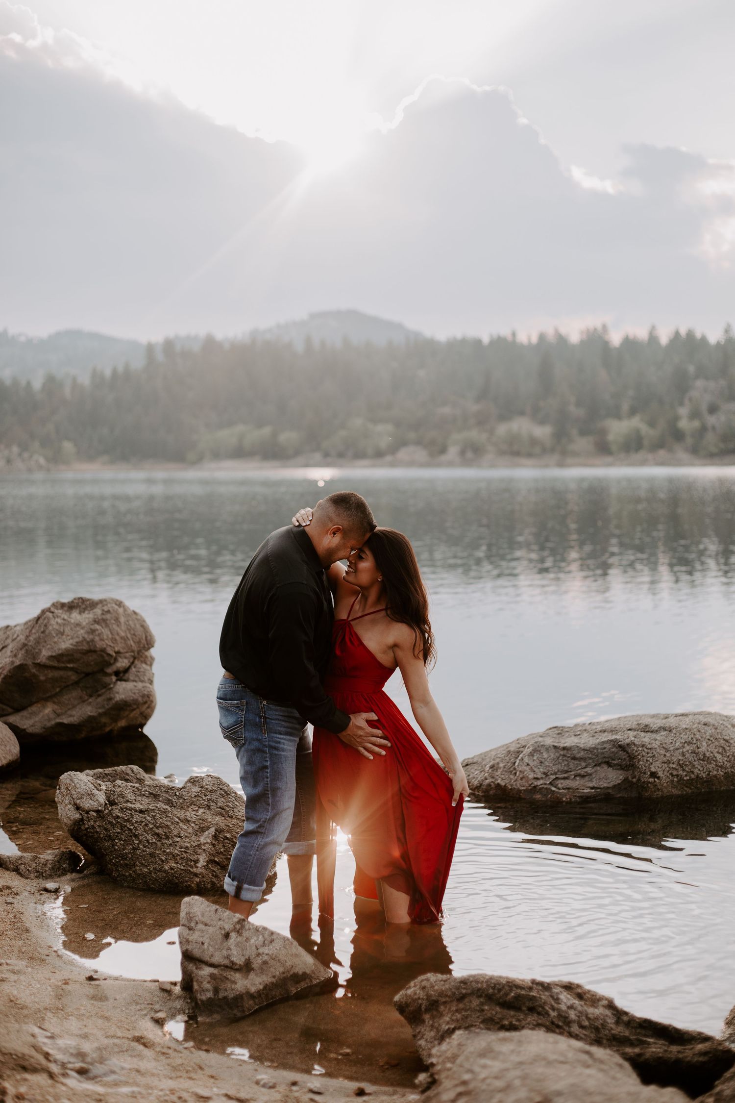 A romantic lakeside sunset photo with a couple embracing among rocky shores.