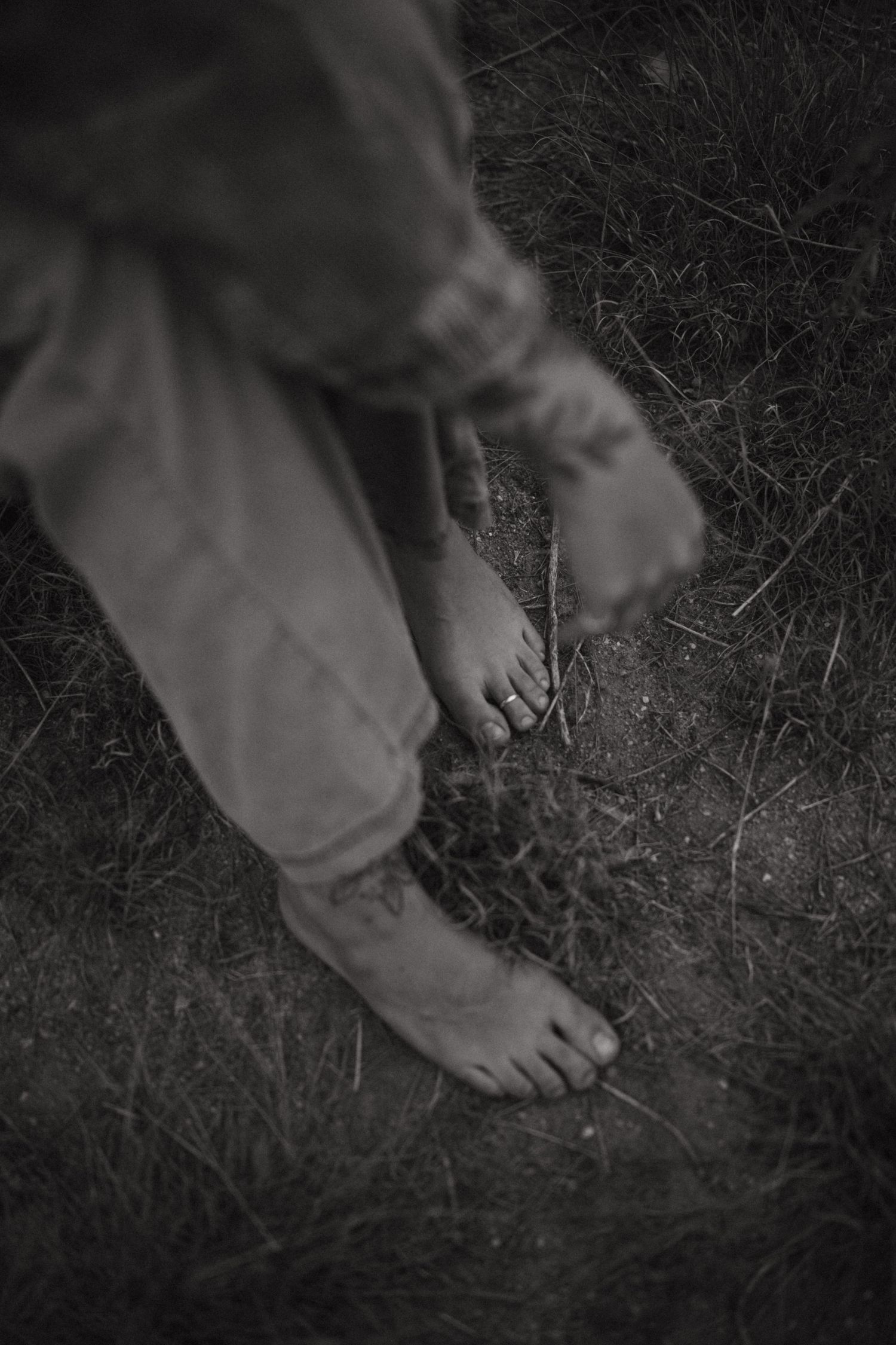 Black and white photo of bare feet on grass with rolled up pants legs showing.
