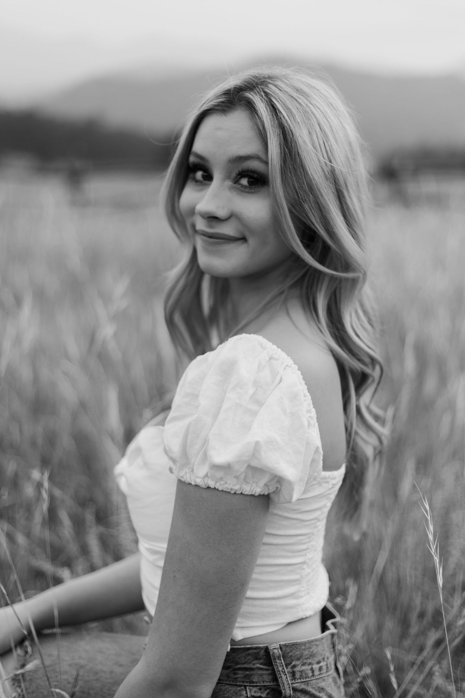 Portrait series in a grassy field wearing white top and denim in black and white.