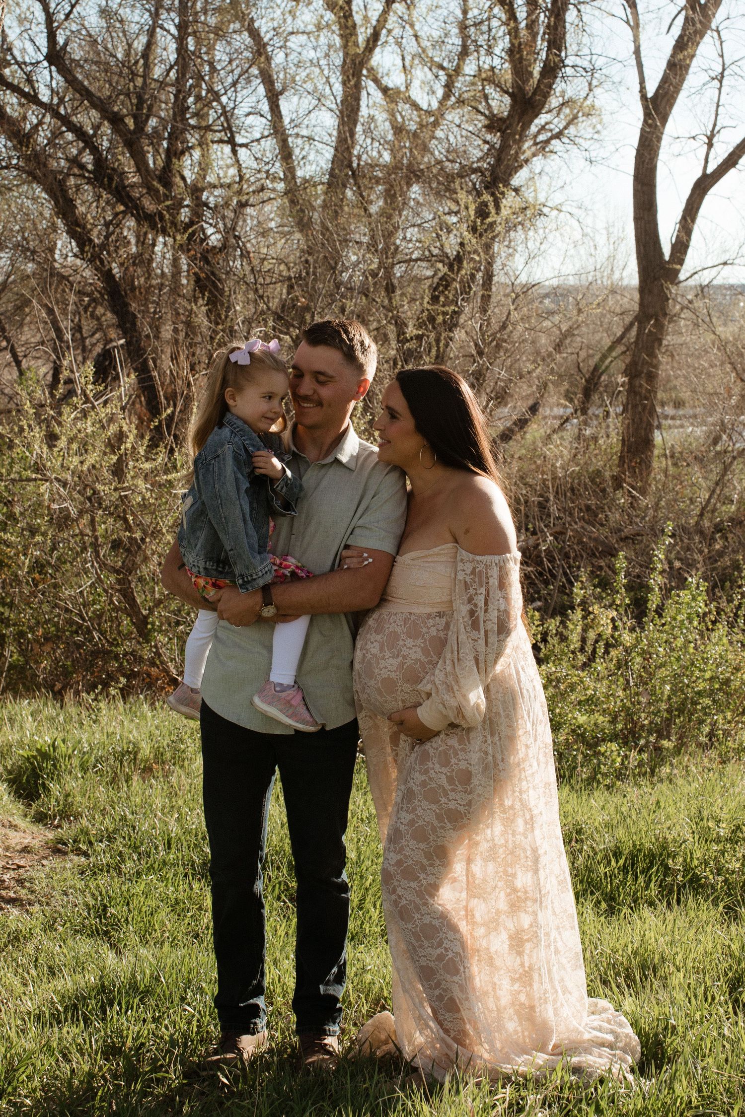 A family poses together in a natural setting with trees and spring foliage.