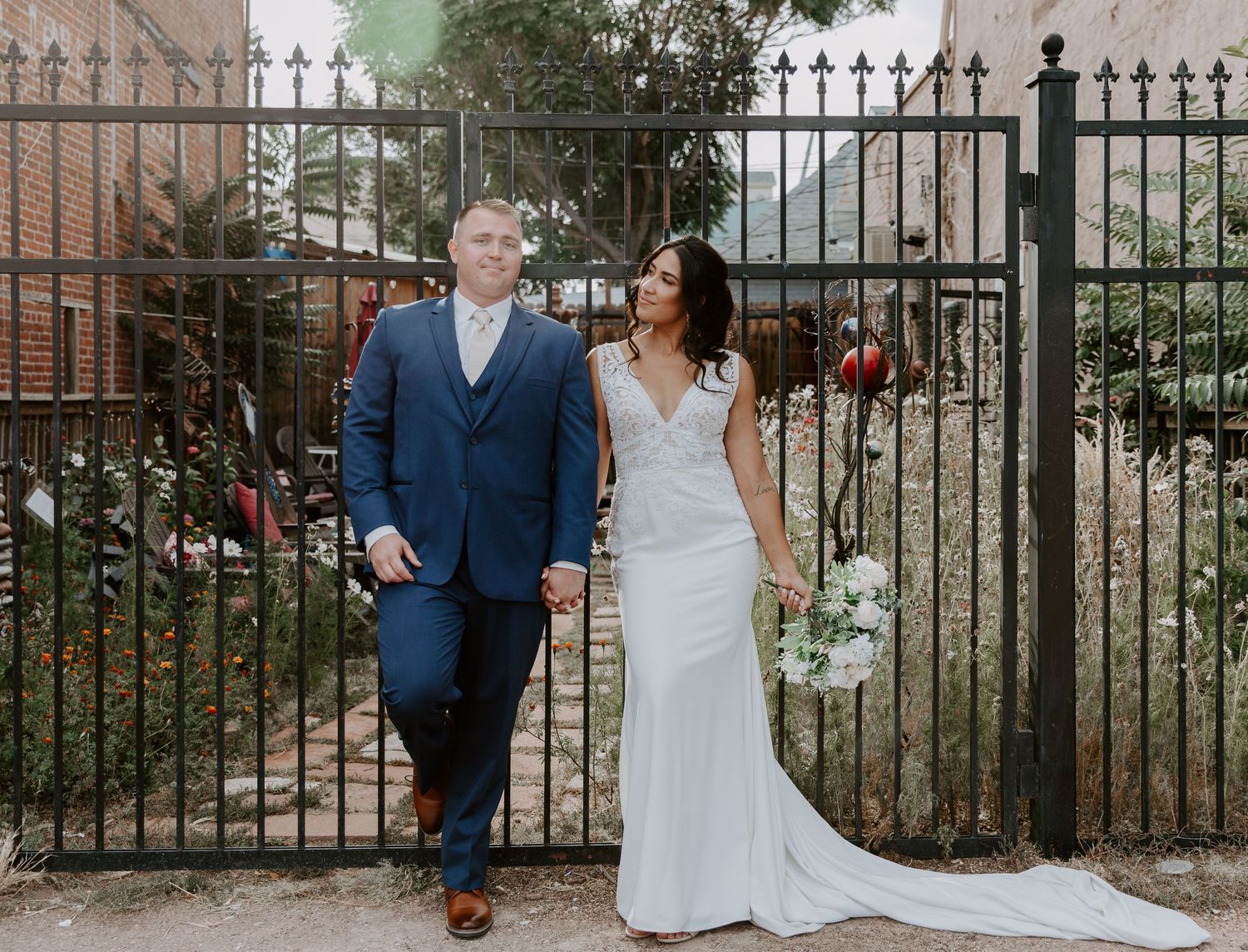 Wedding couple poses together in front of ornate iron fence gate.