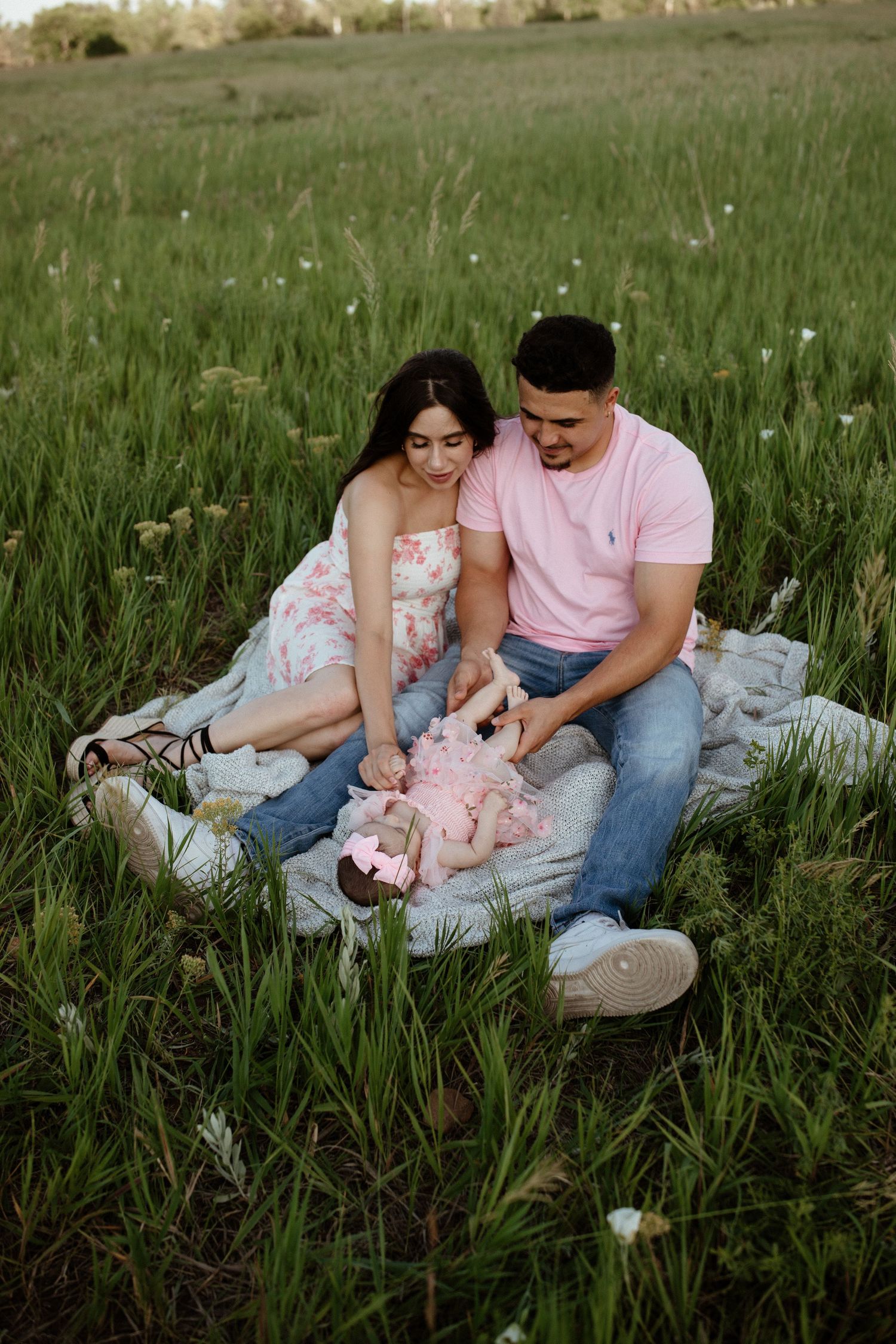 Couple sitting on blanket with baby in flowering meadow at dusk.