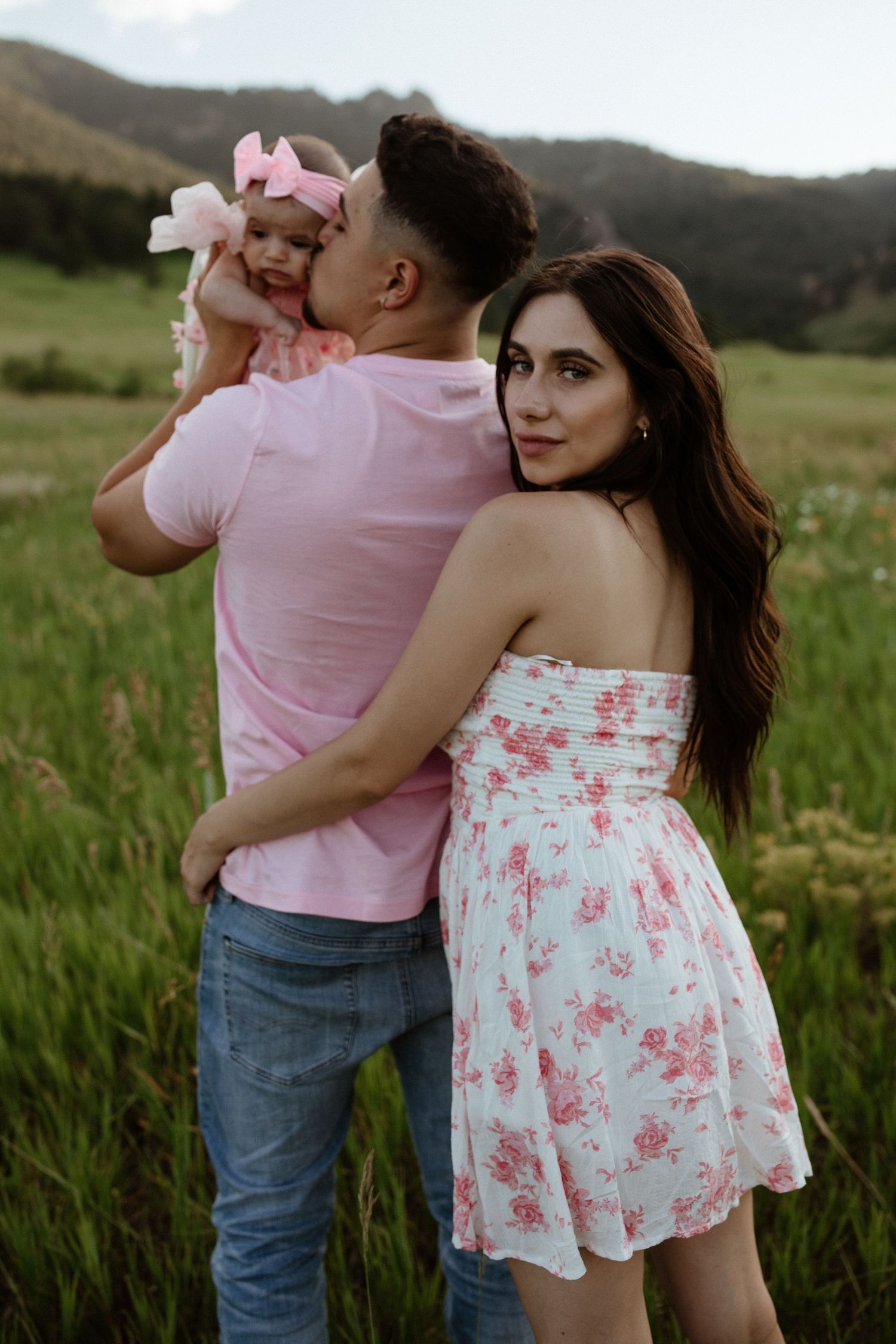 Family in coordinating pink outfits poses together in mountain field at sunset.